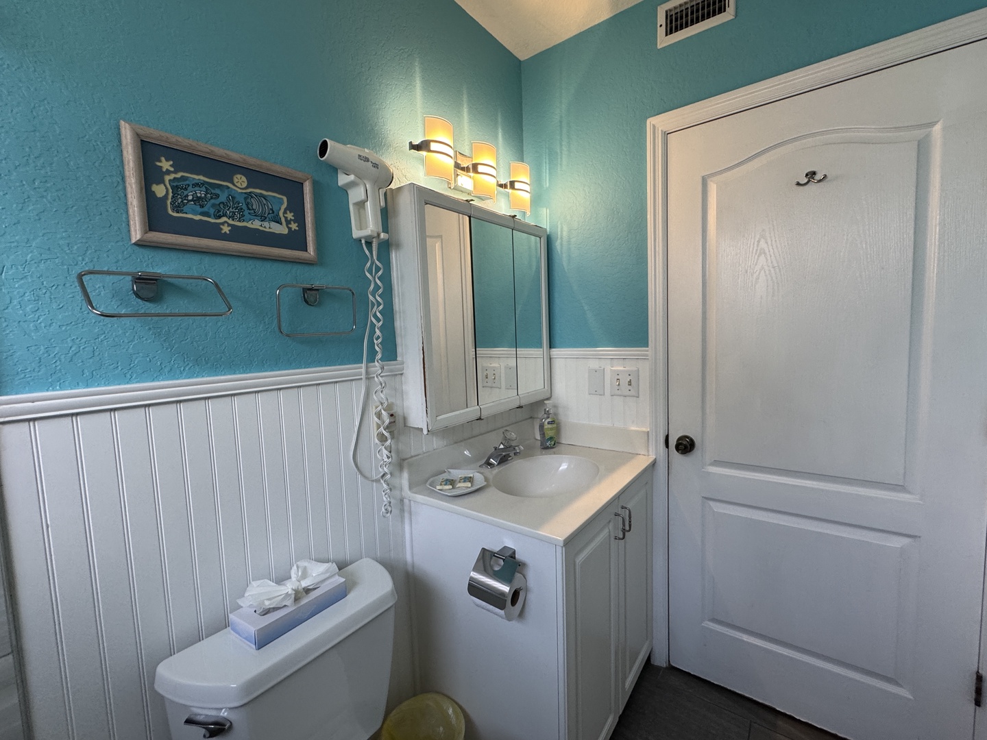 Freshen up in your private bathroom, where coastal turquoise walls and crisp white wainscoting create a bright, beach-inspired retreat—complete with a vanity, mirror, and everything you need to feel at home.