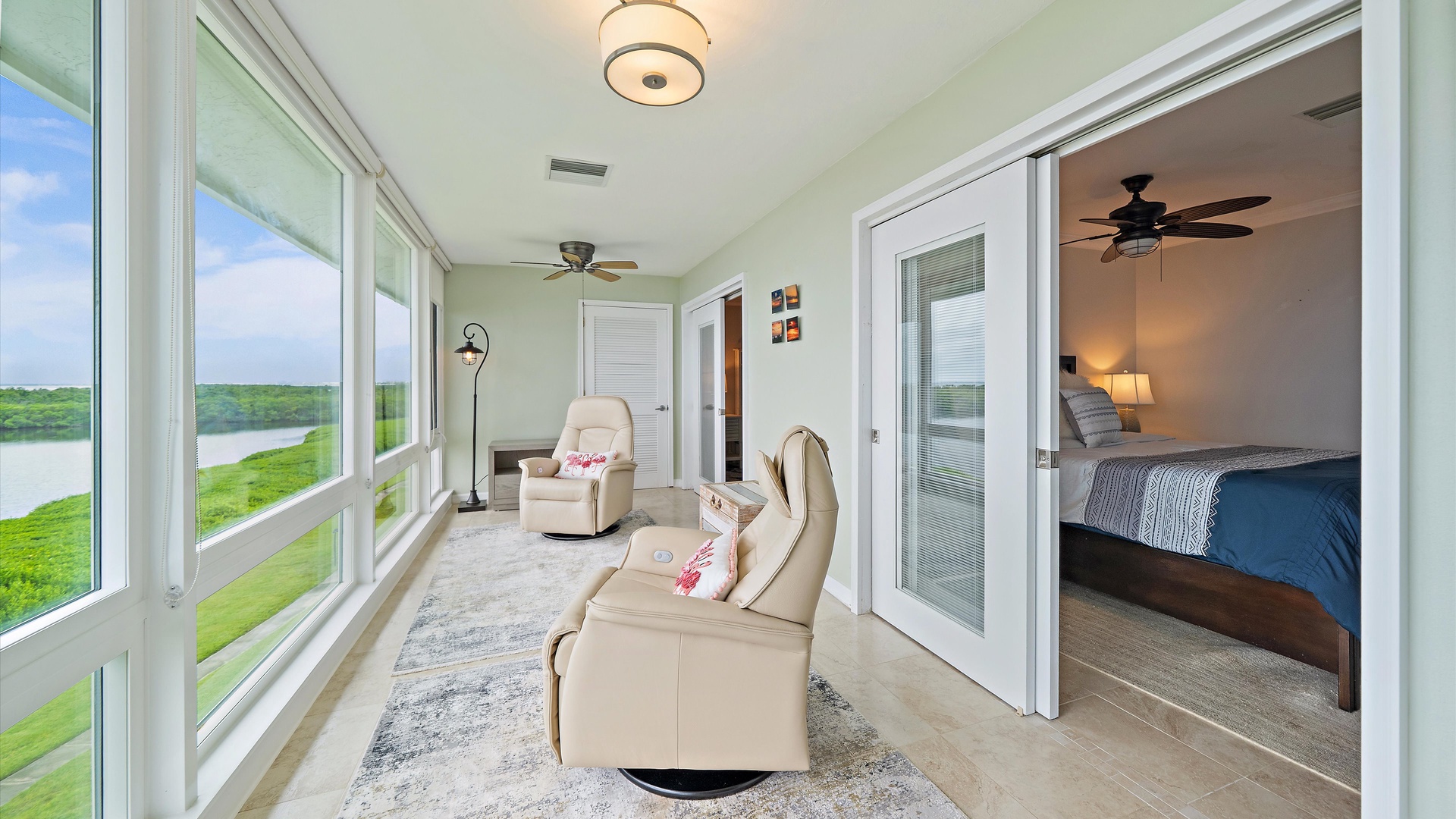 The enclosed sunroom adds a separate waterfront sitting area to the penthouse. Two recliners face a long wall of windows overlooking Sarasota Bay and the mangrove shoreline.