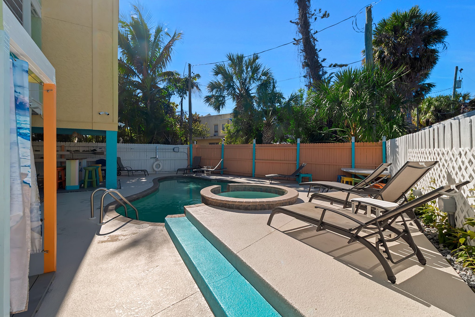 Soak up the sunshine in your private outdoor retreat, featuring a sparkling pool and bubbling hot tub surrounded by tropical palms and comfortable loungers—perfect for unwinding after a day at the beach.
