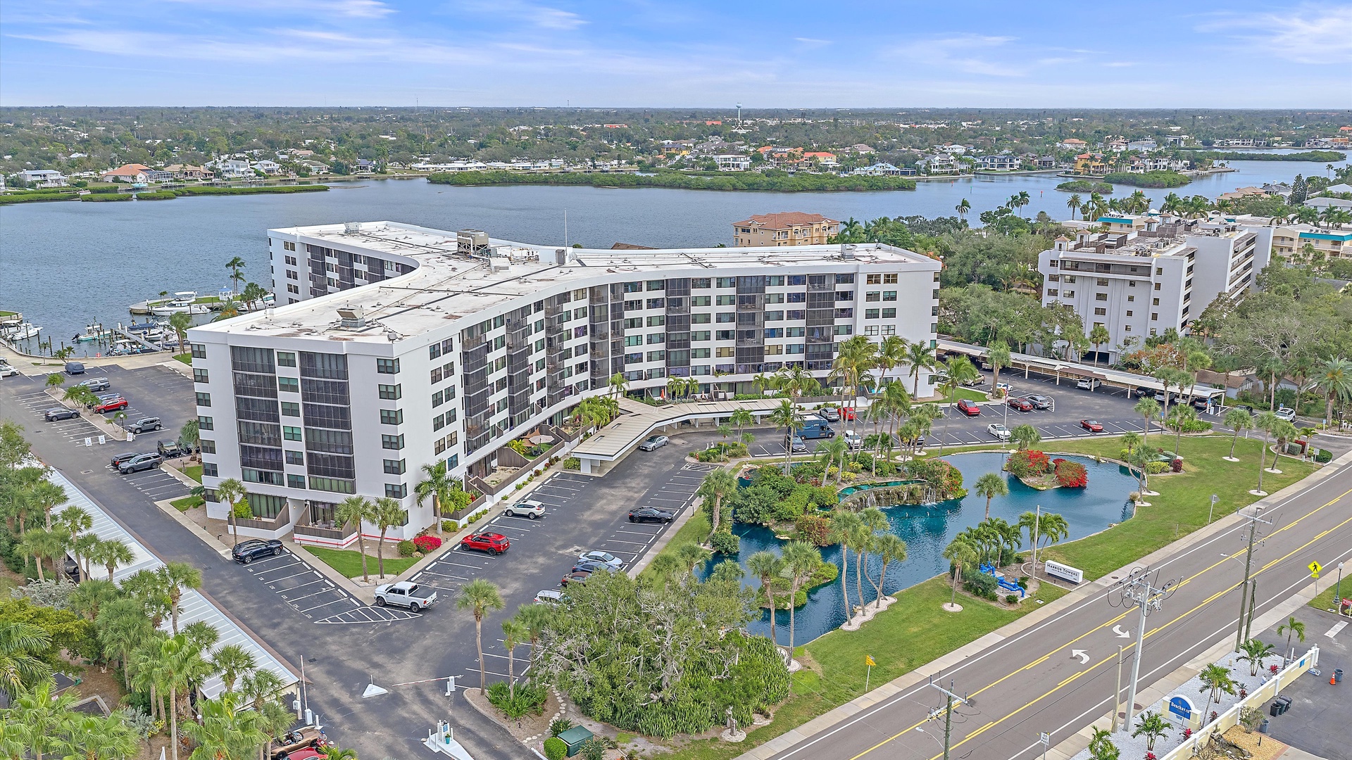 Aerial view of the property complex situated near a scenic waterway, surrounded by palm trees and landscaped grounds in a tropical setting.