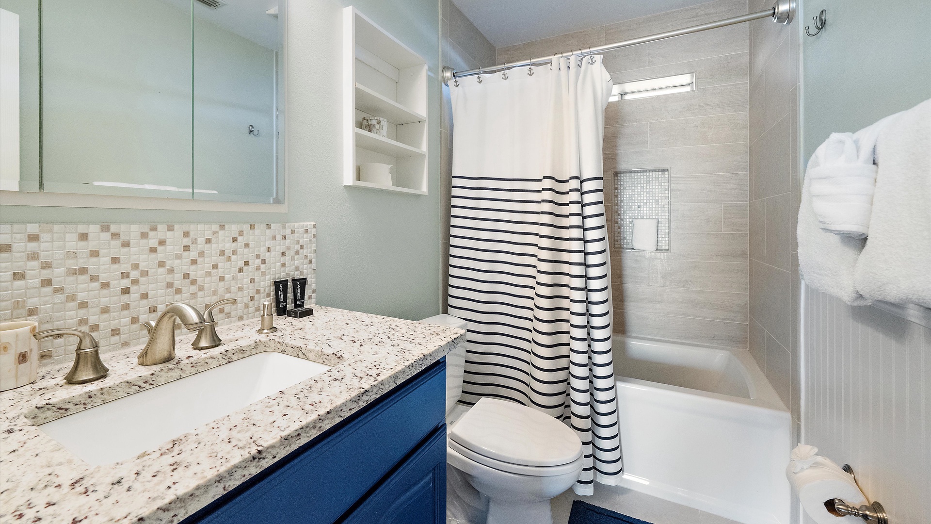 Navy cabinetry, a granite vanity, and a striped shower curtain bring coastal character to the second bathroom. A tub-and-shower combination rounds out this bright, welcoming space.