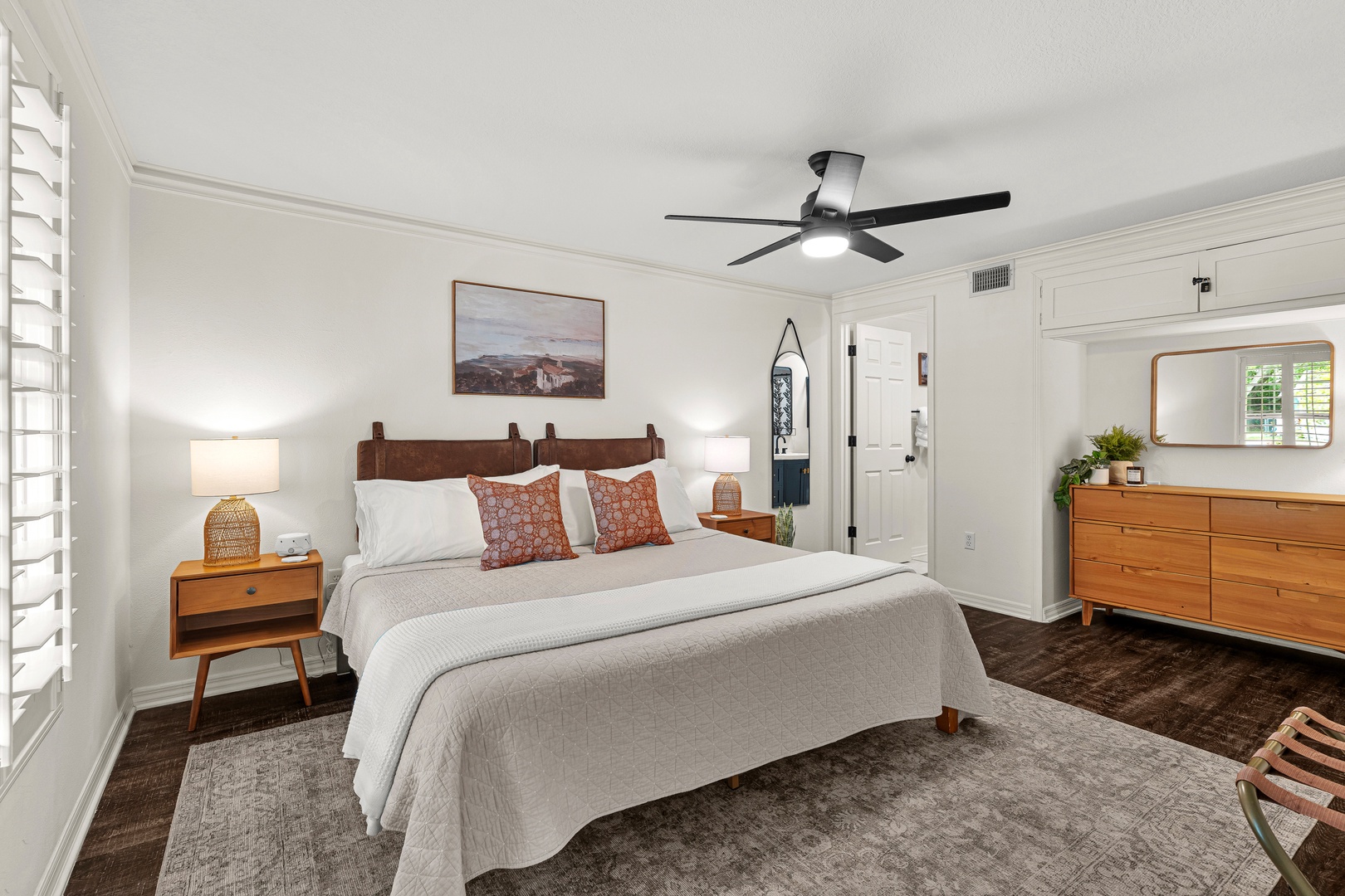 Unwind in your peaceful retreat, featuring a plush bed with stylish linens, warm wood furnishings, soft lighting, and a ceiling fan to keep you comfortable year-round.