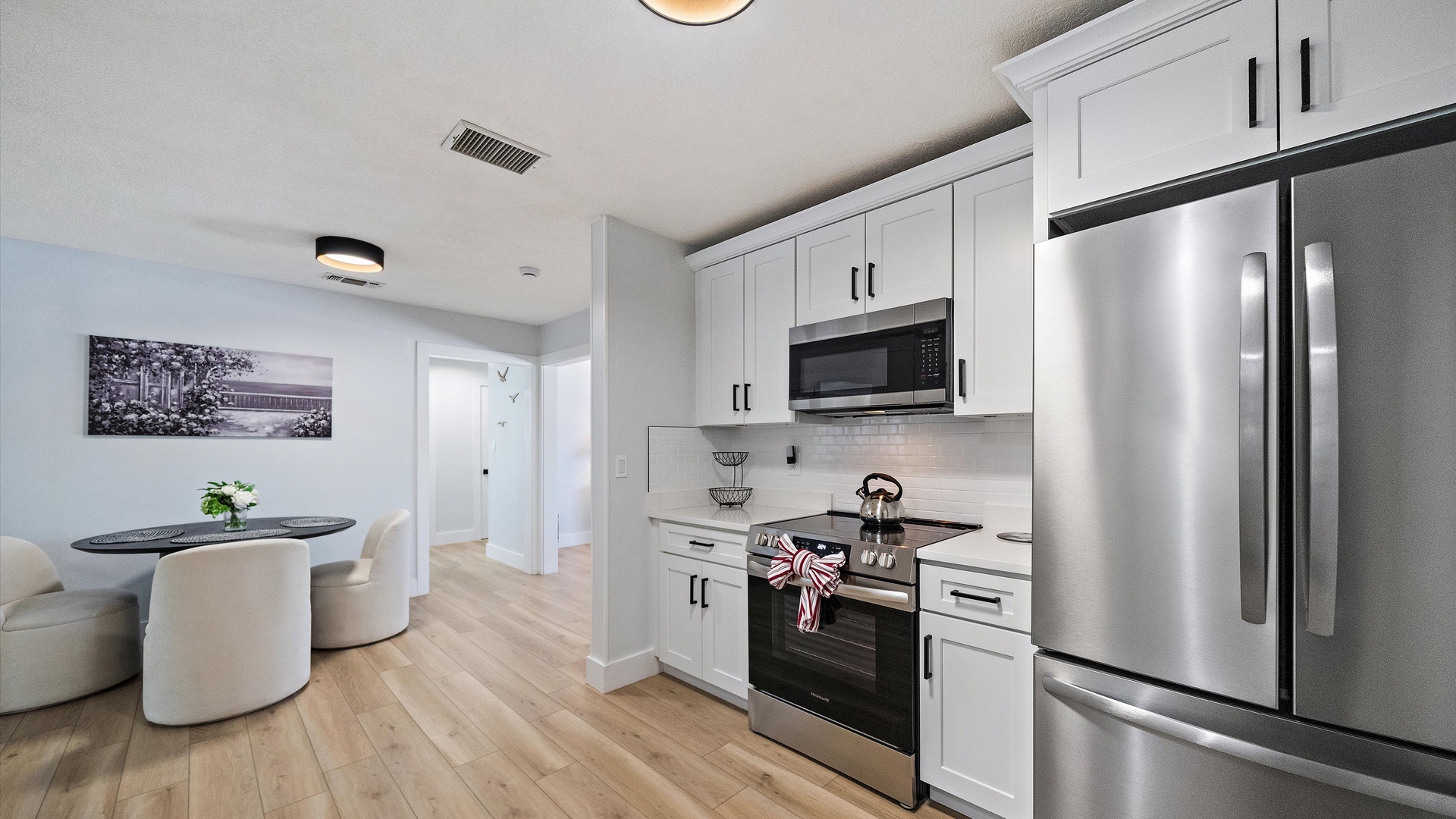 Your modern kitchen features sleek stainless appliances, bright white cabinetry, and warm wood floors that flow seamlessly into your dining space—perfect for cooking and gathering.