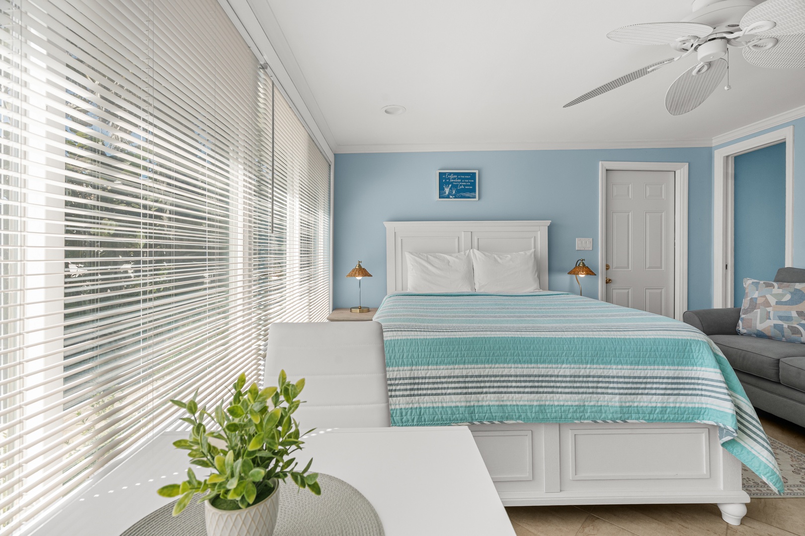 Sink into coastal comfort in your serene bedroom with calming blue walls and bright natural light streaming through the blinds.