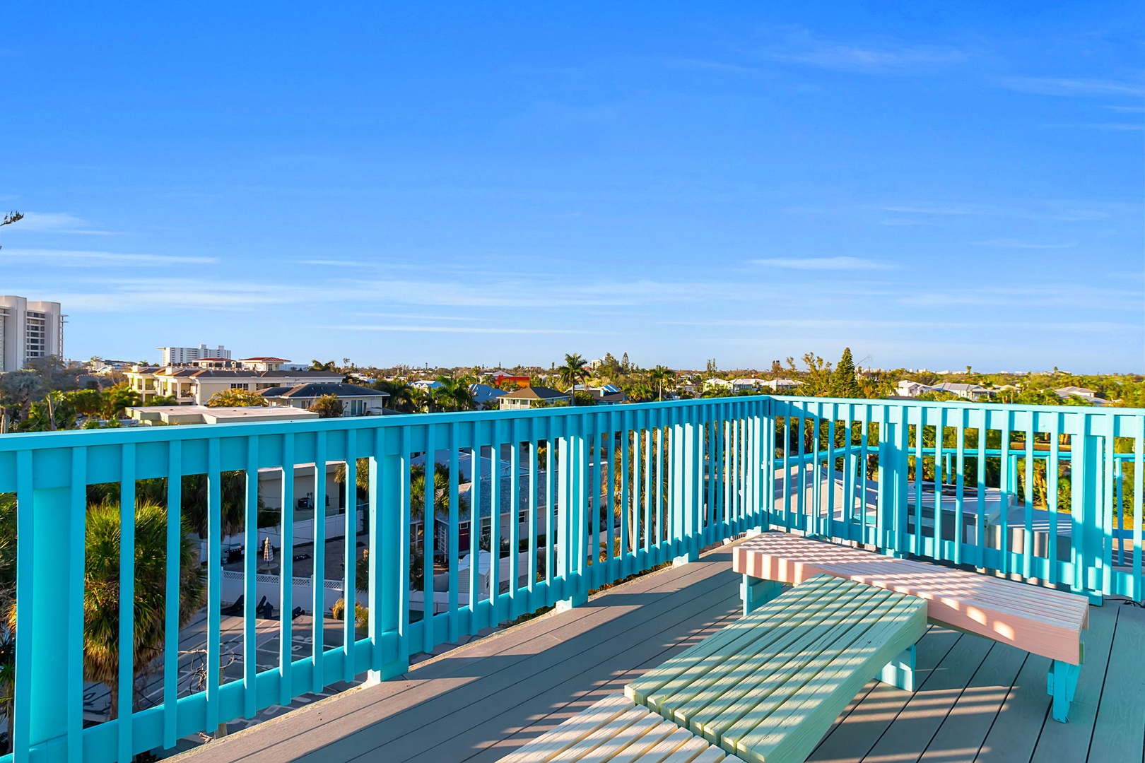 Bright turquoise railings frame this rooftop terrace overlooking the neighborhood—a sunny spot to lounge and soak in the views under clear blue skies.
