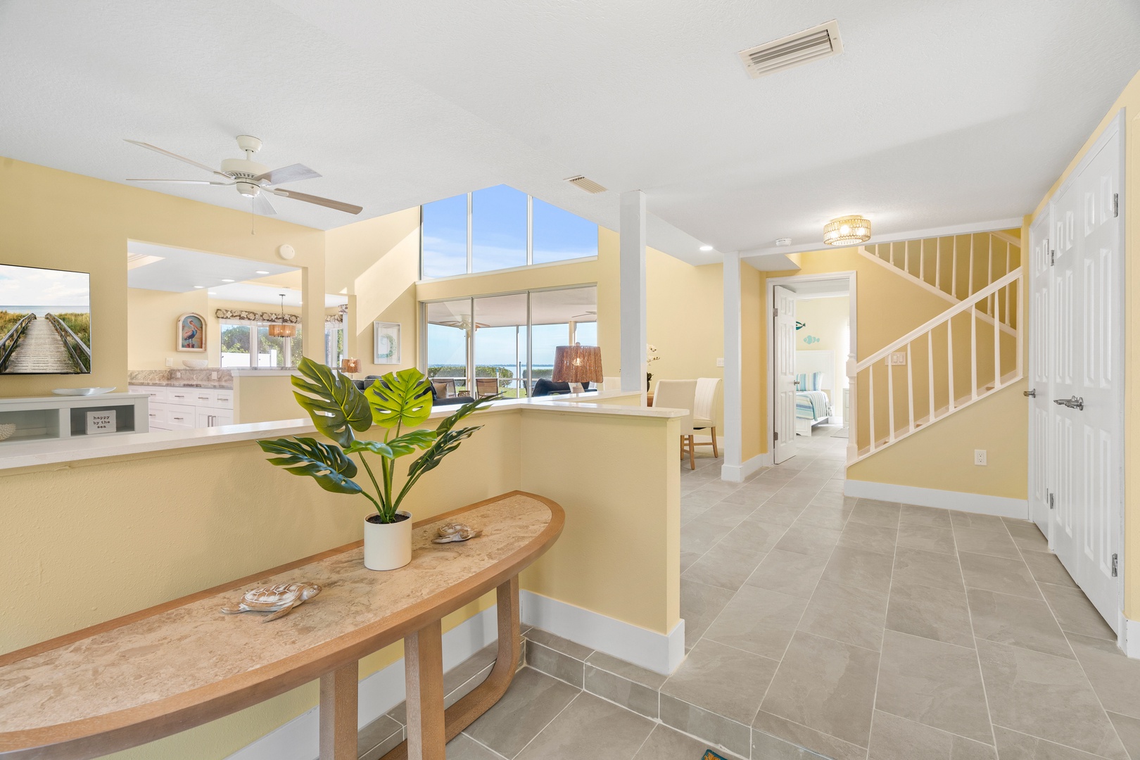 Step into your bright, open living space where vaulted ceilings and tropical plant accents create a welcoming coastal retreat atmosphere.