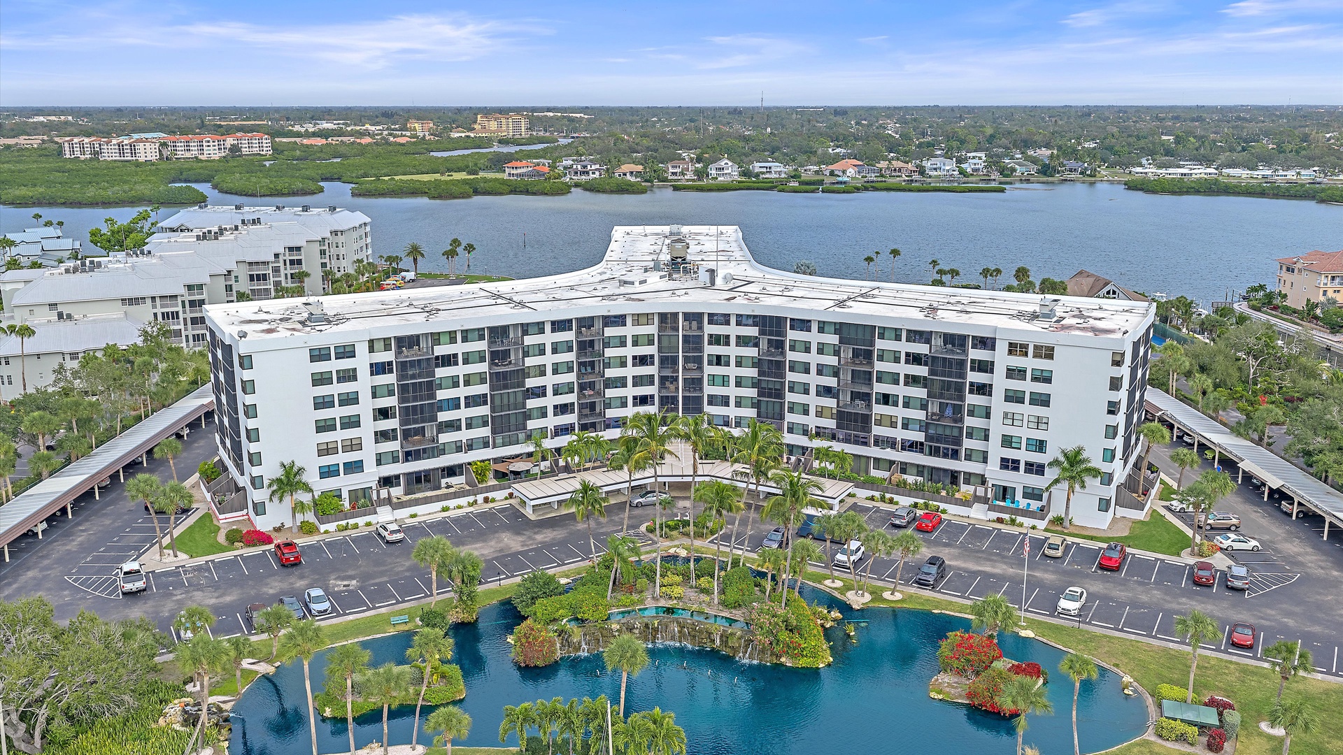Aerial view of the property featuring a distinctive curved white building complex with waterfront positioning and landscaped grounds in a tropical setting.