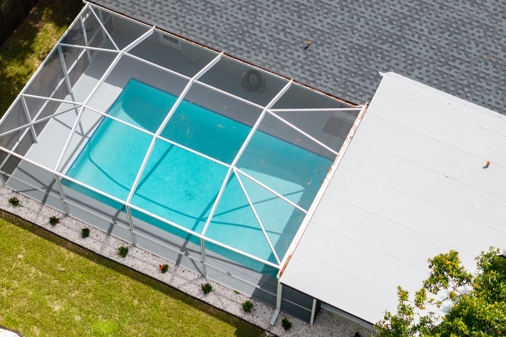 Aerial view of the property featuring a screened-in pool area with crystal-clear waters and manicured landscaping.
