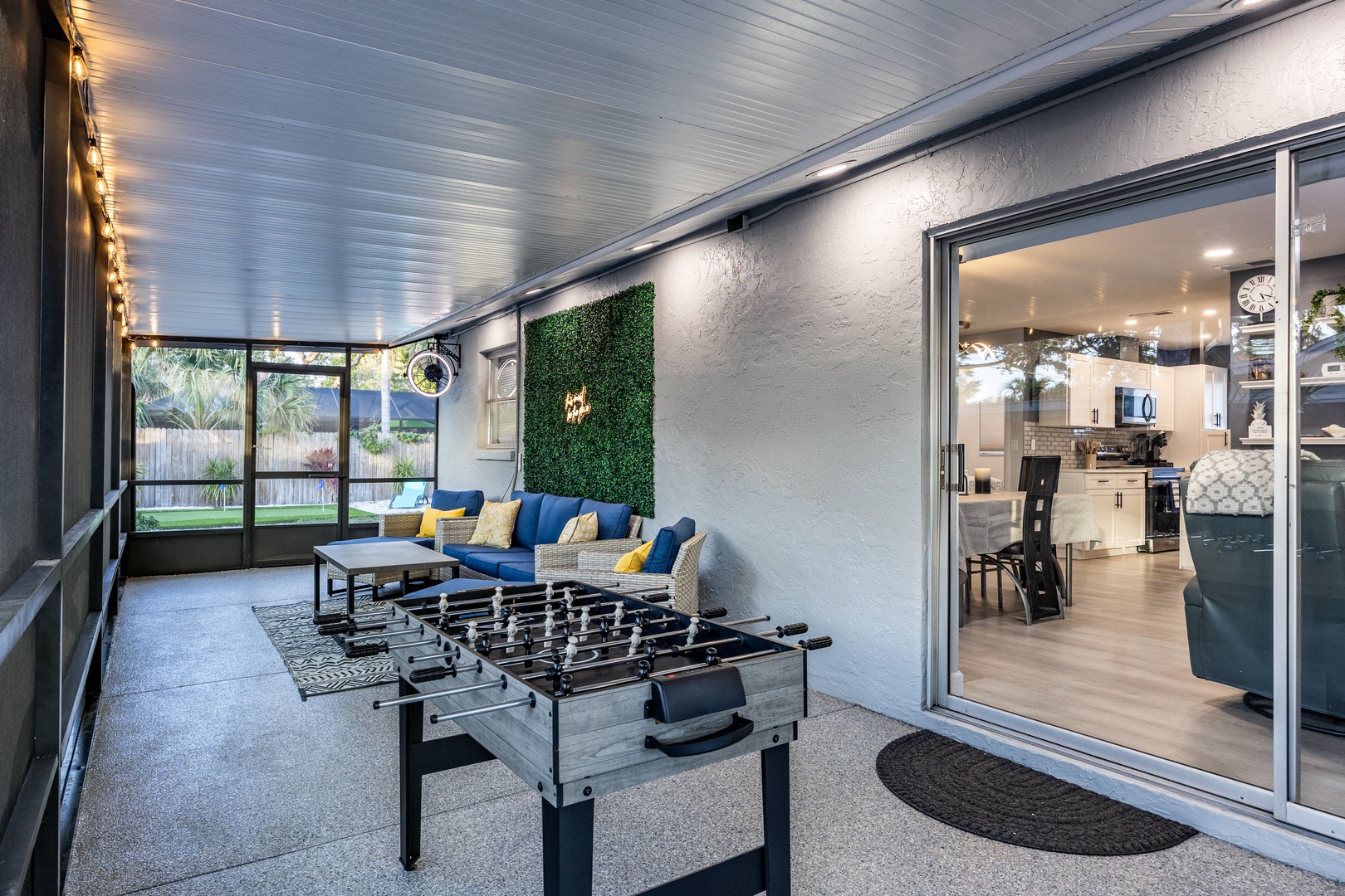 Your covered patio blends indoor comfort with outdoor living, featuring a foosball table and cozy seating under twinkling string lights.