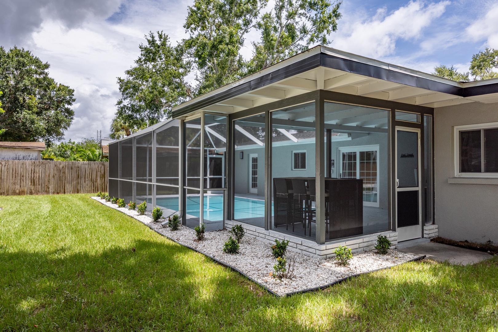 Modern glass-enclosed pool area with pristine lawn and mature trees creating a private backyard oasis.