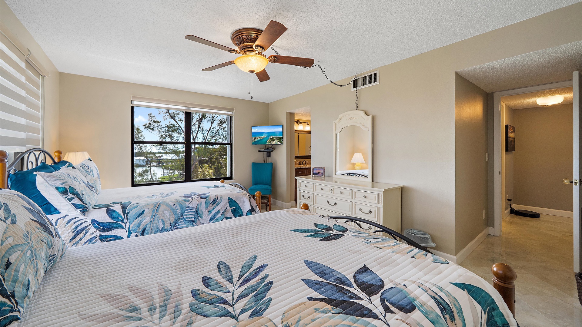 Unwind in your coastal-themed bedroom with twin beds, ceiling fan, and peaceful tree views from your private window.