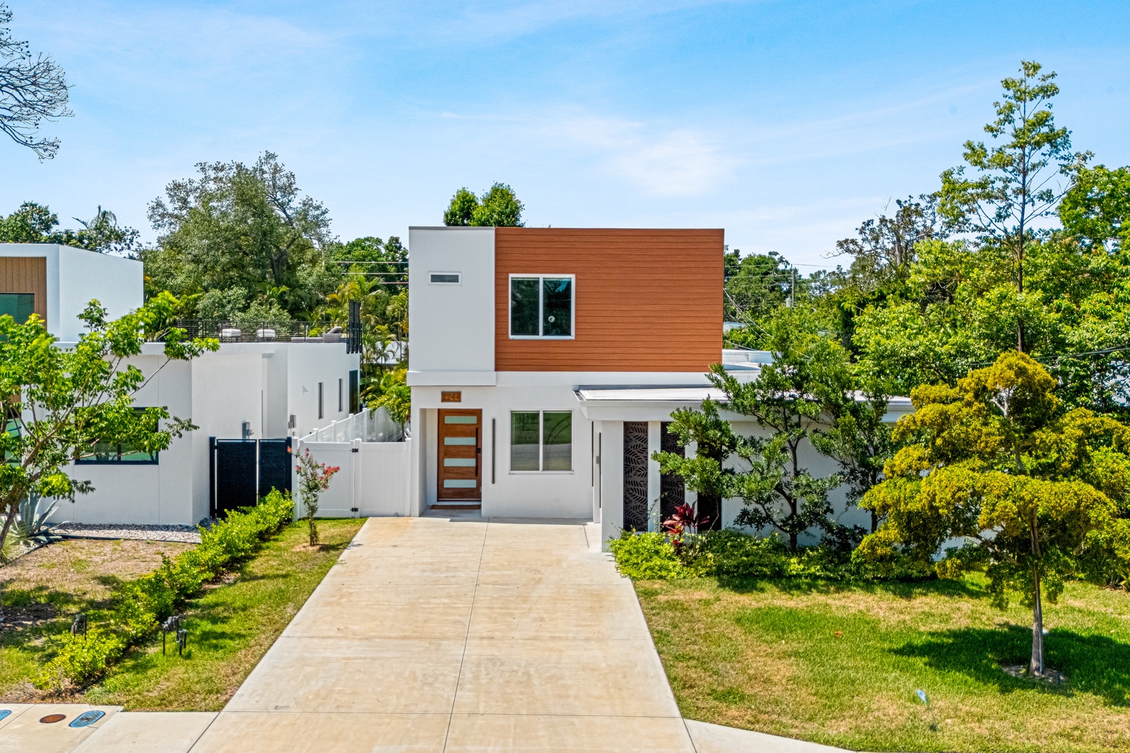 A modern two-story home featuring sleek white and warm wood accents, nestled in a tranquil, tree-lined neighborhood with private parking.
