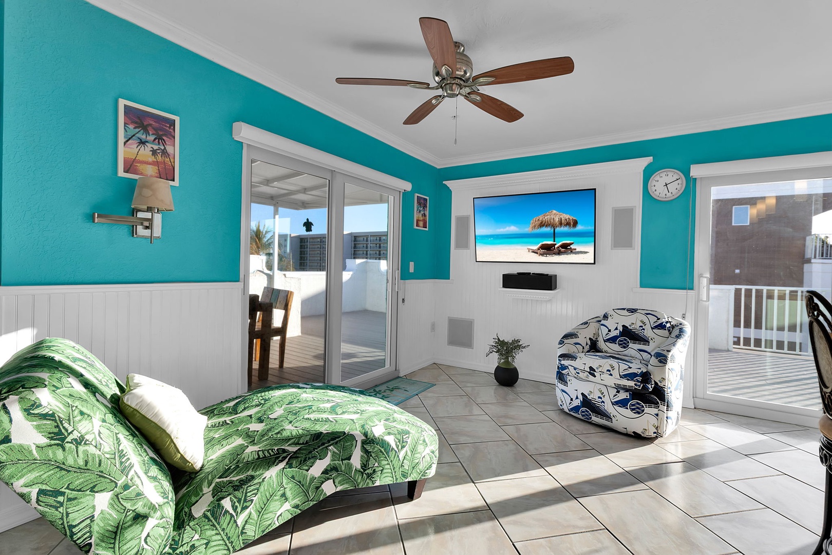 Step into your bright, tropical-inspired living space with vibrant turquoise walls and easy balcony access. Relax in the coastal-themed seating while natural light fills the room.