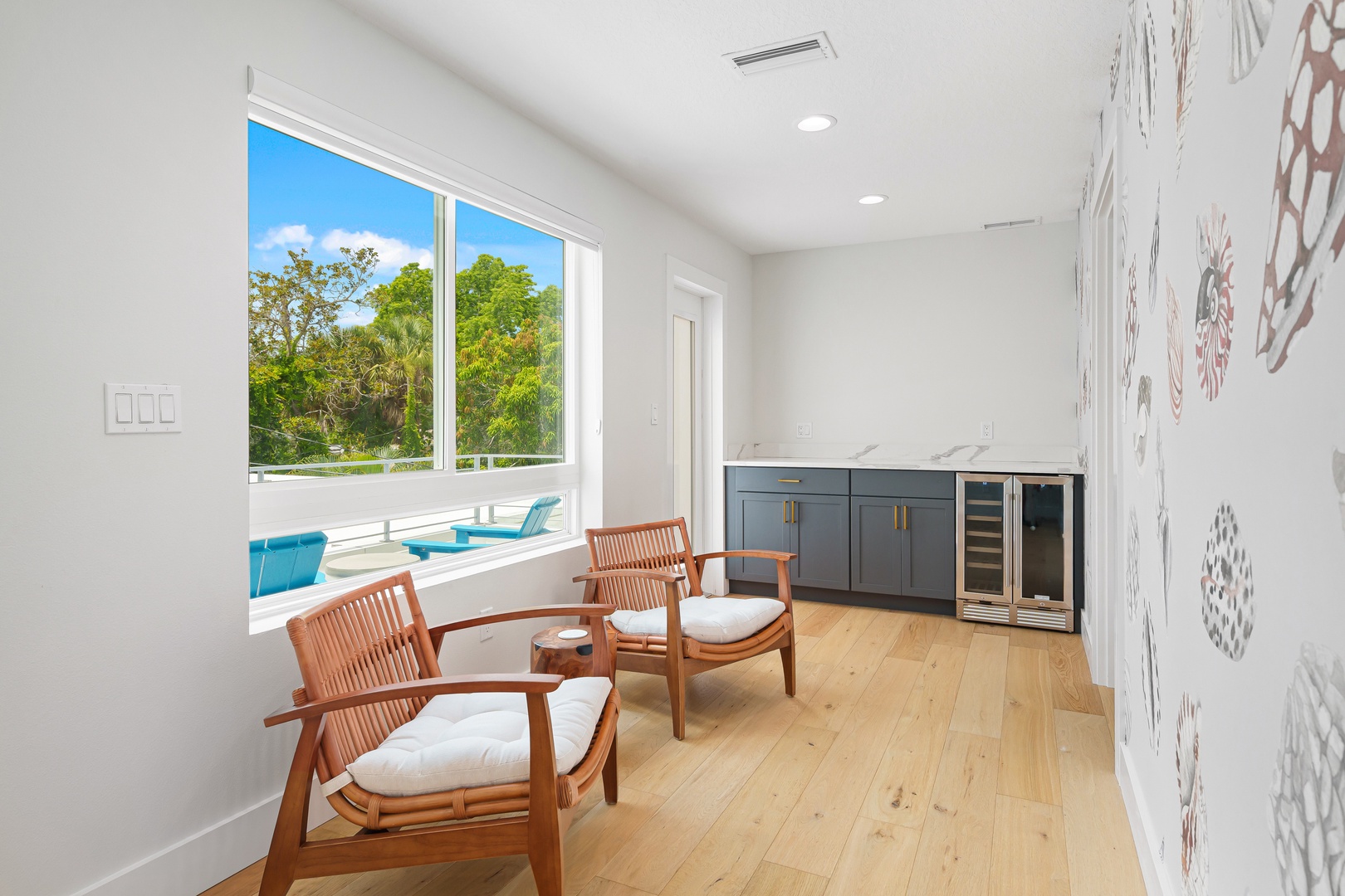Relax in your stylish seating area with a refreshing beverage from the wine fridge, while warm wood tones and poolside views create the perfect spot to unwind and soak in the sunlit atmosphere.