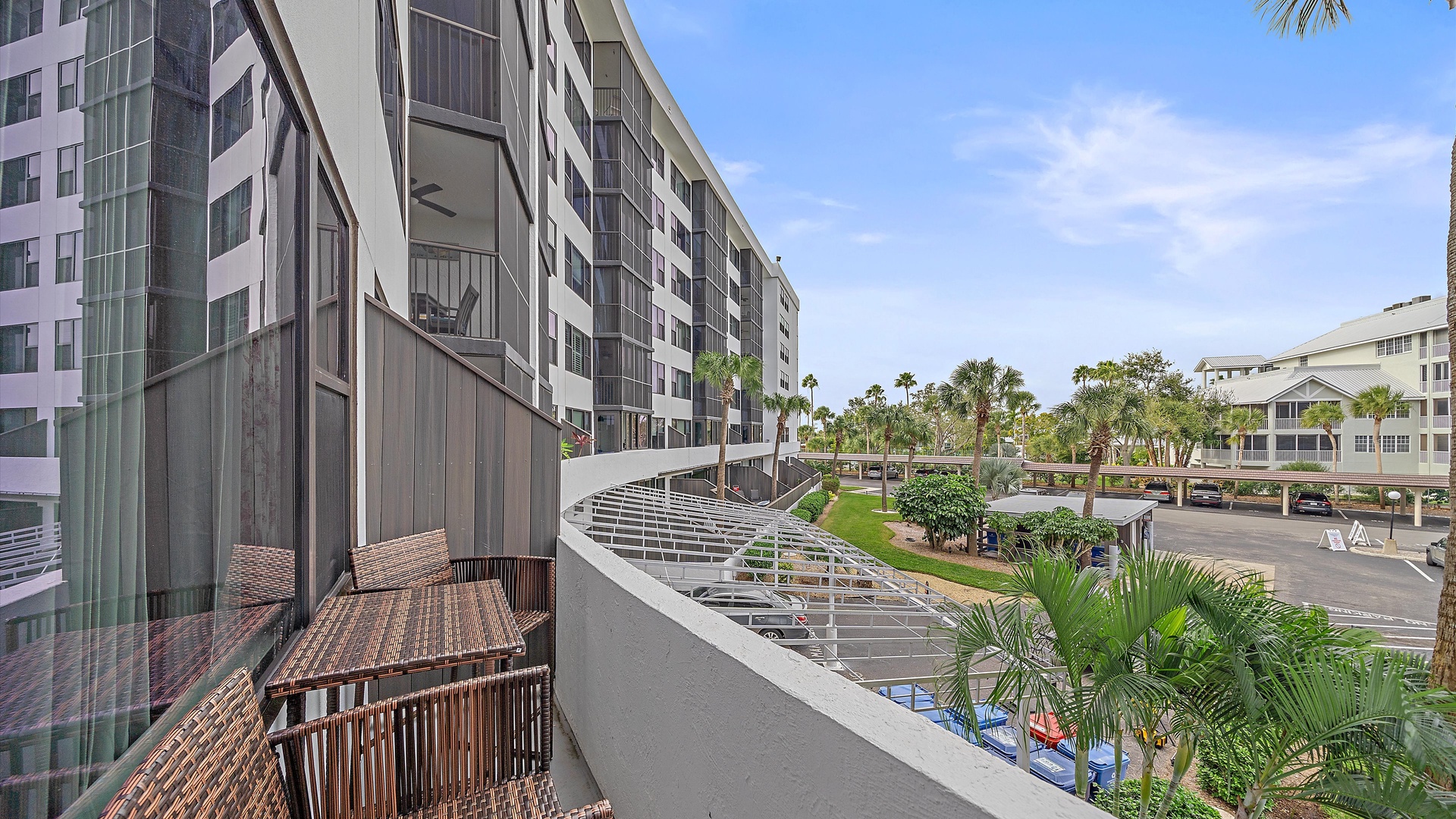 Spacious balcony with outdoor seating overlooking tropical landscaped grounds and neighboring buildings in this resort-style community.