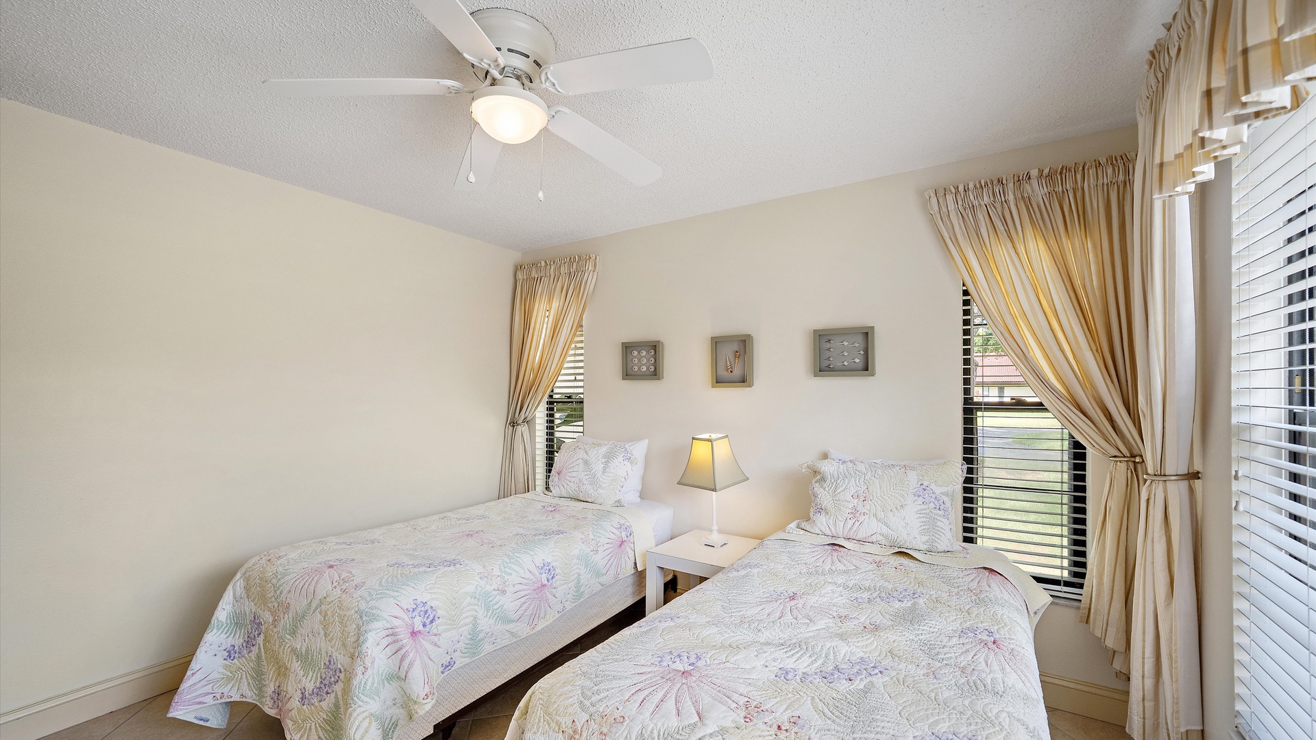 Relax in your peaceful bedroom with two comfortable beds, soft natural light filtering through elegant curtains, and a ceiling fan to keep you cool during your stay.