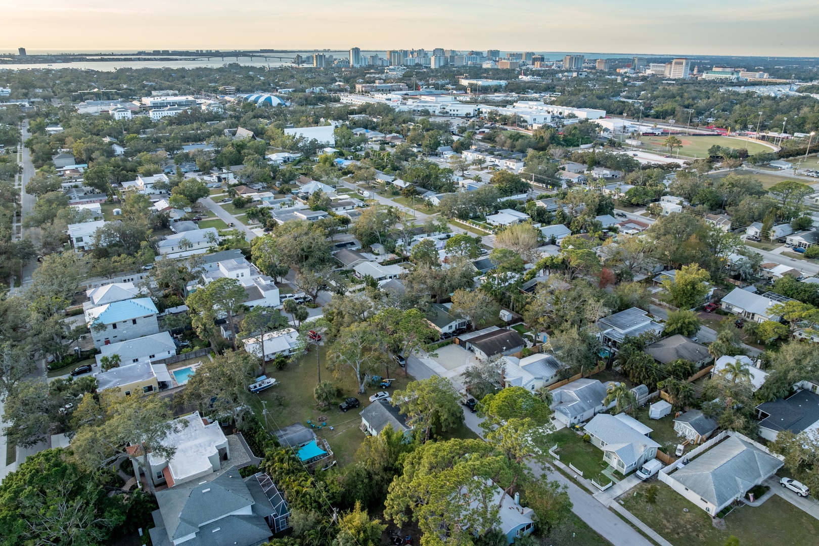 Aerial view showcasing the peaceful residential neighborhood with tree-lined streets and the vibrant city skyline visible in the distance.