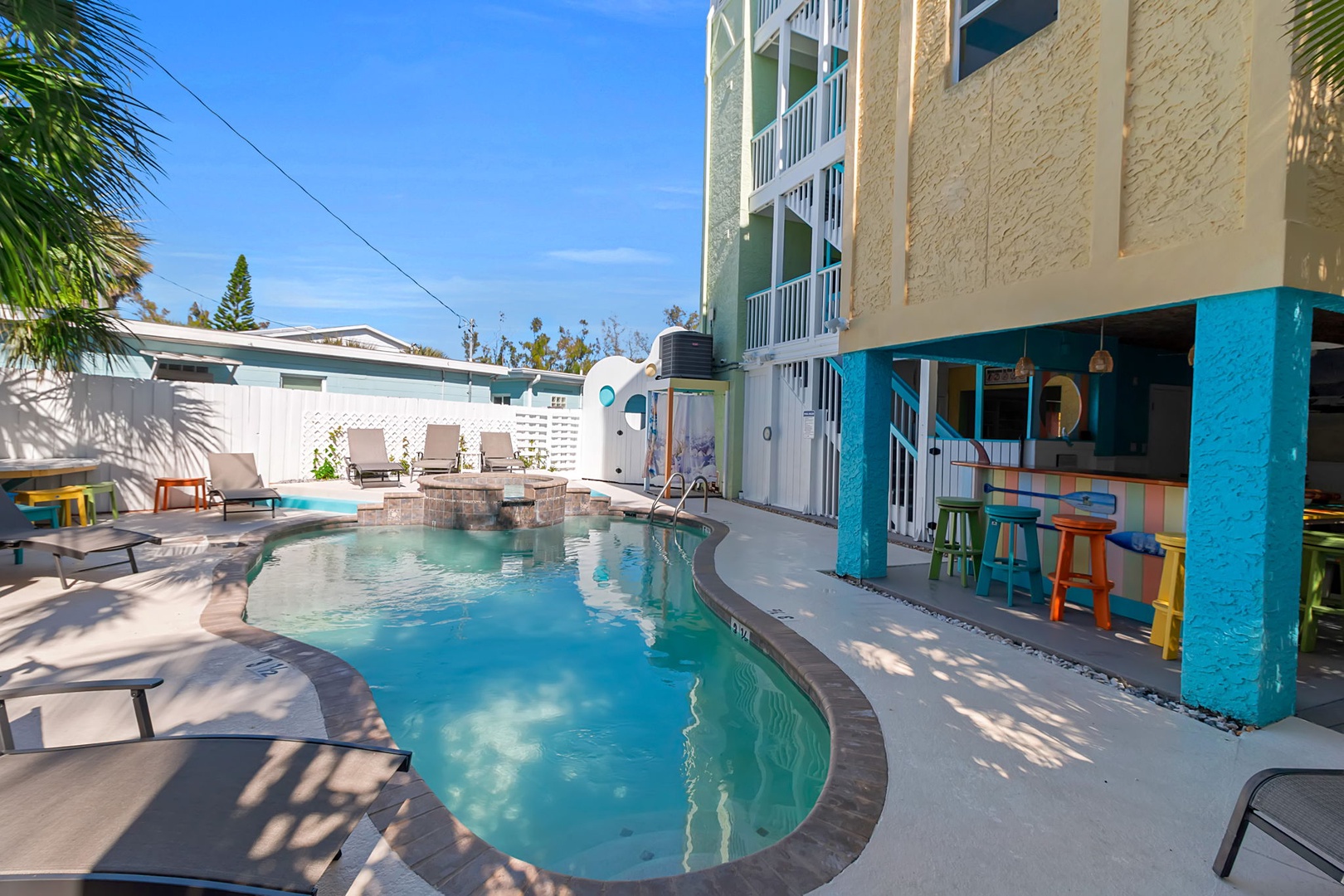 The sparkling pool curves invitingly through the sunny courtyard, with colorful poolside bar seating and plenty of lounge chairs waiting for your perfect beach day.