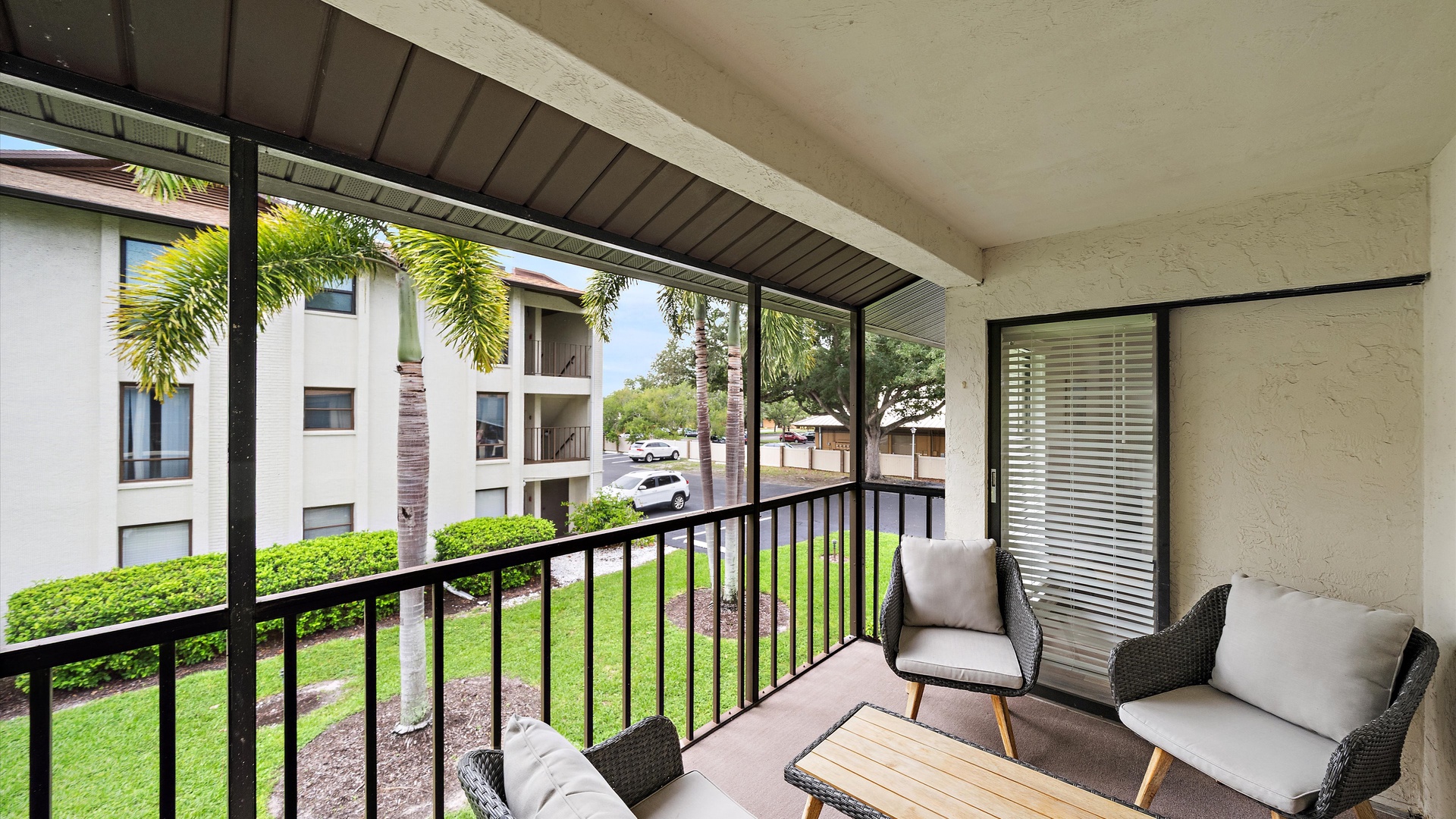 A covered balcony where you can unwind with morning coffee or evening relaxation, overlooking lush landscaping and tropical palms framing peaceful neighborhood views.