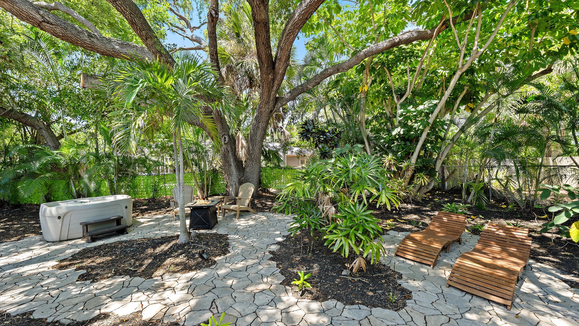 A tranquil garden oasis featuring a private hot tub beneath towering palms and tropical greenery, with shaded pathways perfect for peaceful moments outdoors.