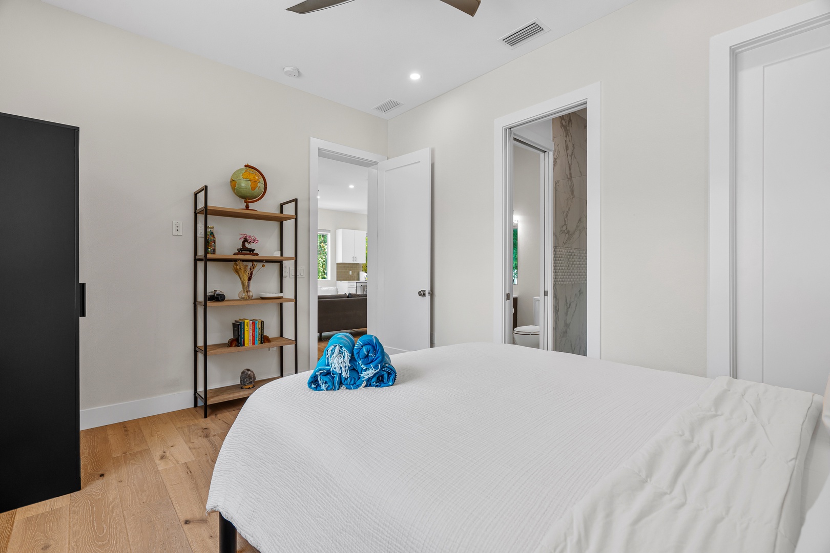 Your bright, peaceful bedroom invites you to unwind with its crisp white linens, warm wood floors, and thoughtful touches like a vintage globe and open shelving. A private ensuite awaits just beyond your door.