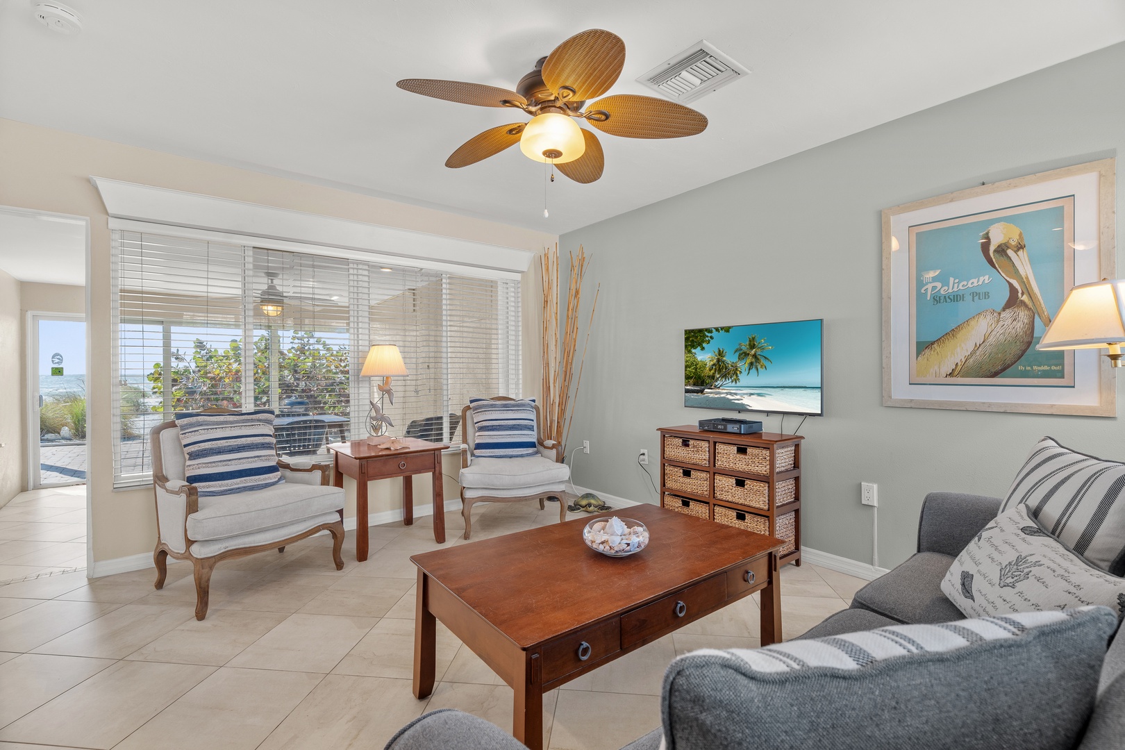 Relax in your coastal-inspired living room with comfortable seating, tropical ceiling fan, and charming nautical decor creating the perfect beach retreat atmosphere.