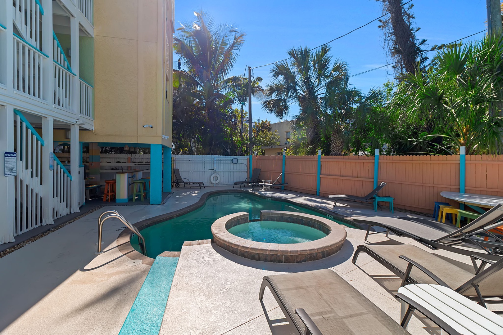 The property features a heated pool and raised hot tub surrounded by tropical palms, with ample lounge seating for sunny afternoons.