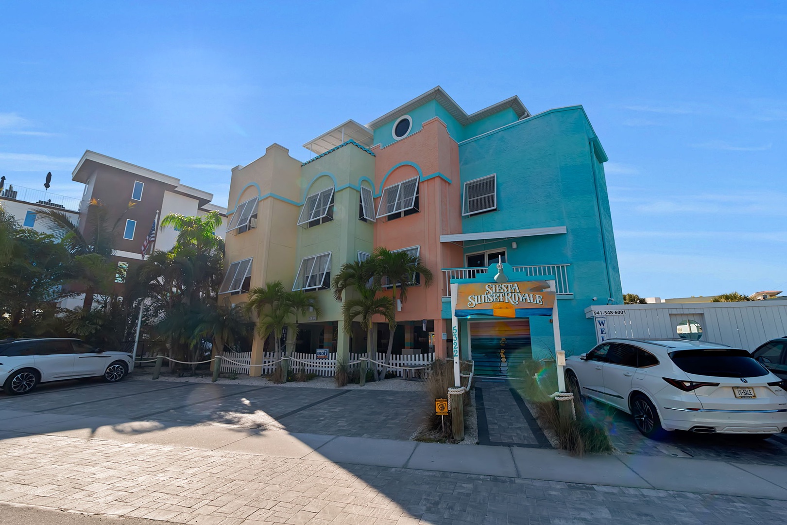 A colorful tropical resort building with vibrant turquoise, coral, and green facades surrounded by lush palm trees marks your arrival to this coastal escape.