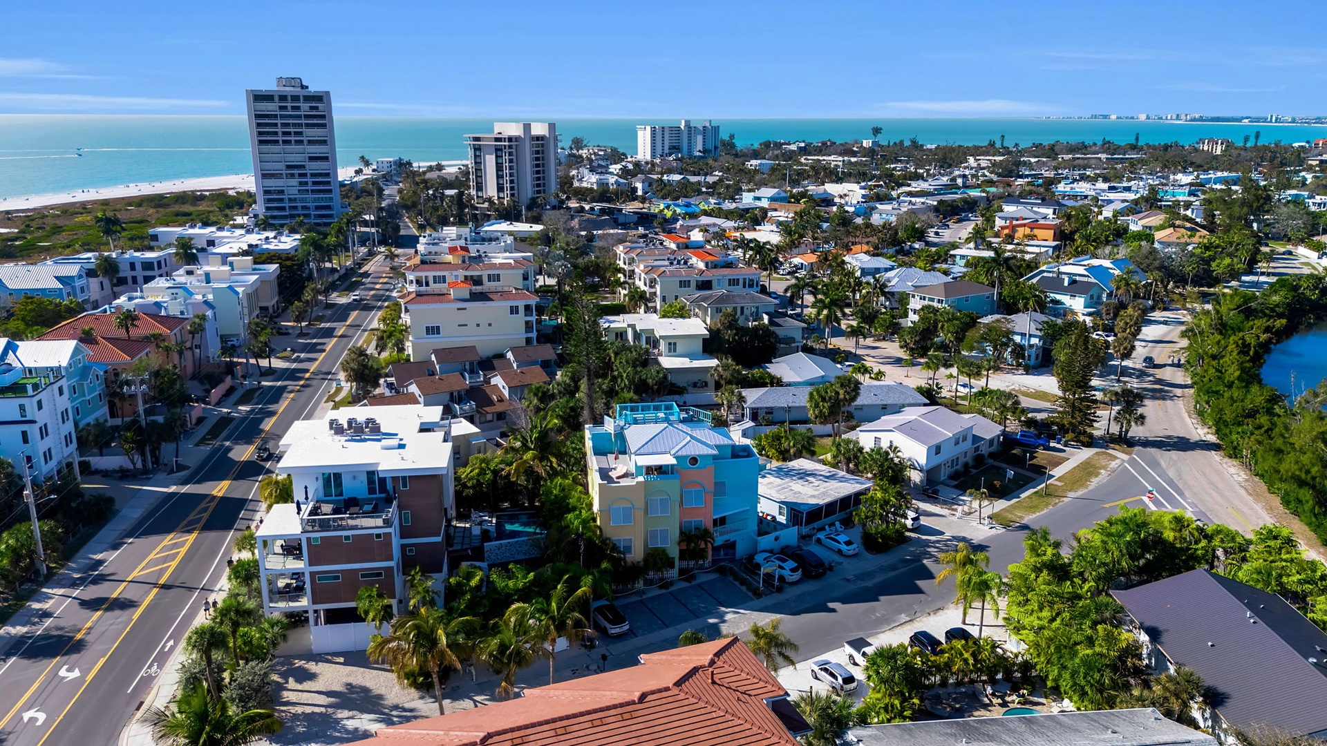 Aerial view of a vibrant beachside neighborhood with coastal streets leading to pristine turquoise waters and sandy shores.