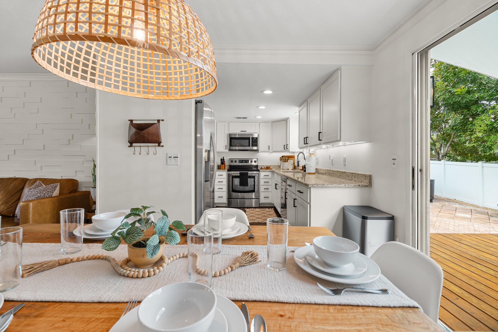 Gather around this welcoming dining table set for your next meal. Bright natural light fills the space, while the open kitchen invites easy meal prep and the patio beckons just beyond.