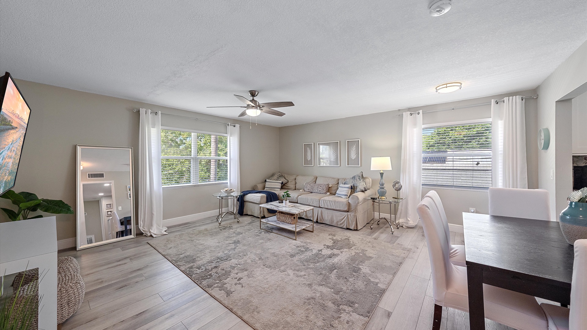 Unwind in your bright, open living space with plush seating, soft natural light streaming through large windows, and ceiling fans for comfort—your perfect spot to relax and feel right at home.