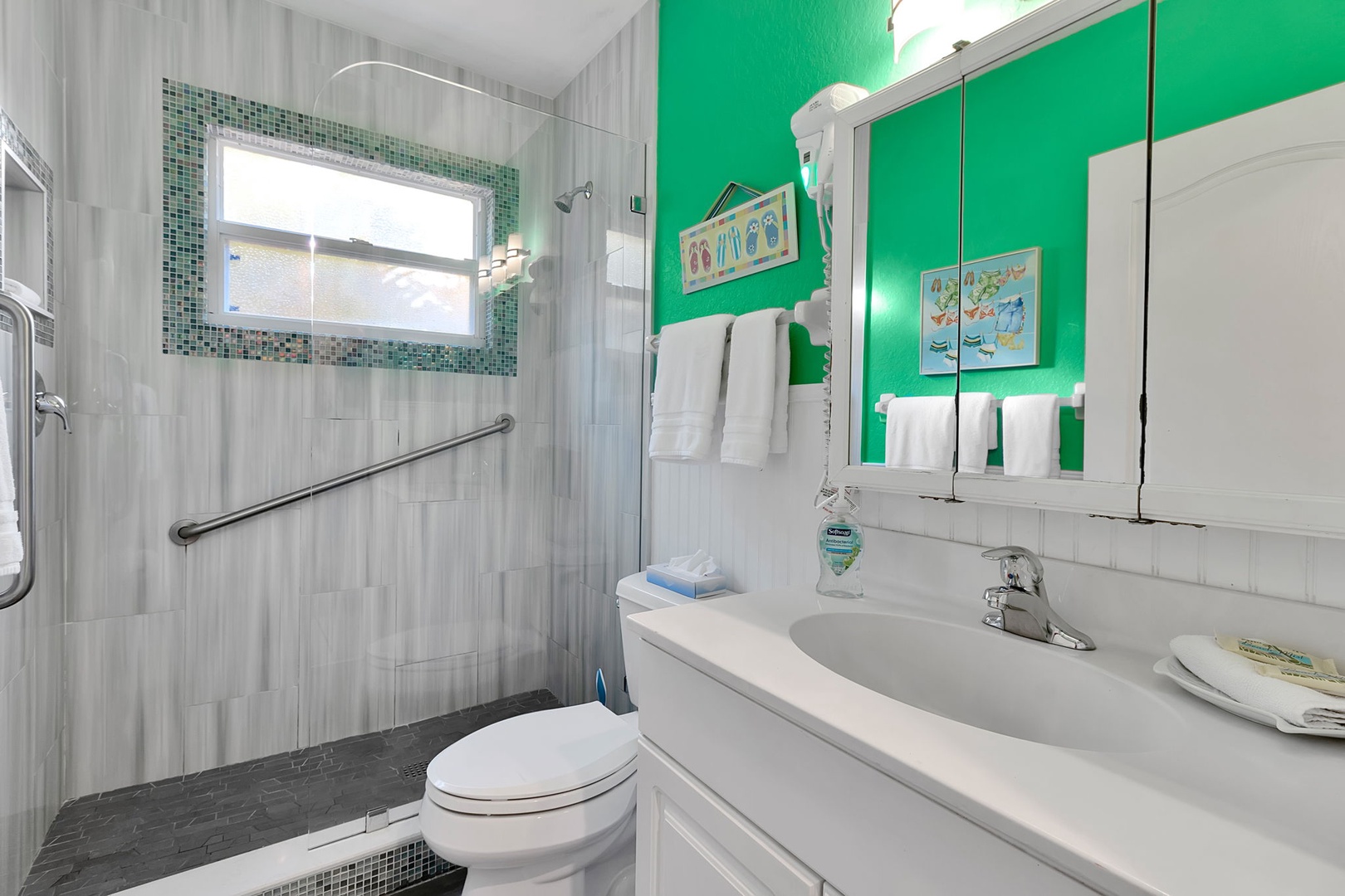 Step into your bright, cheerfully designed bathroom with a spacious walk-in shower and fresh white towels waiting for you. The vibrant green accent wall adds a playful coastal touch to your morning routine.