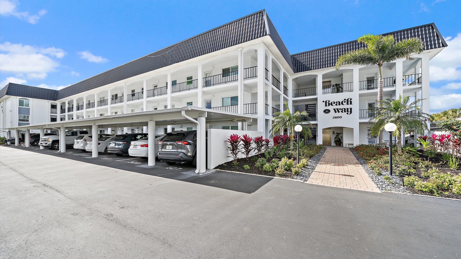 Beach Bay property features modern white architecture with covered parking spaces, tropical landscaping, and clear signage marking the entrance.