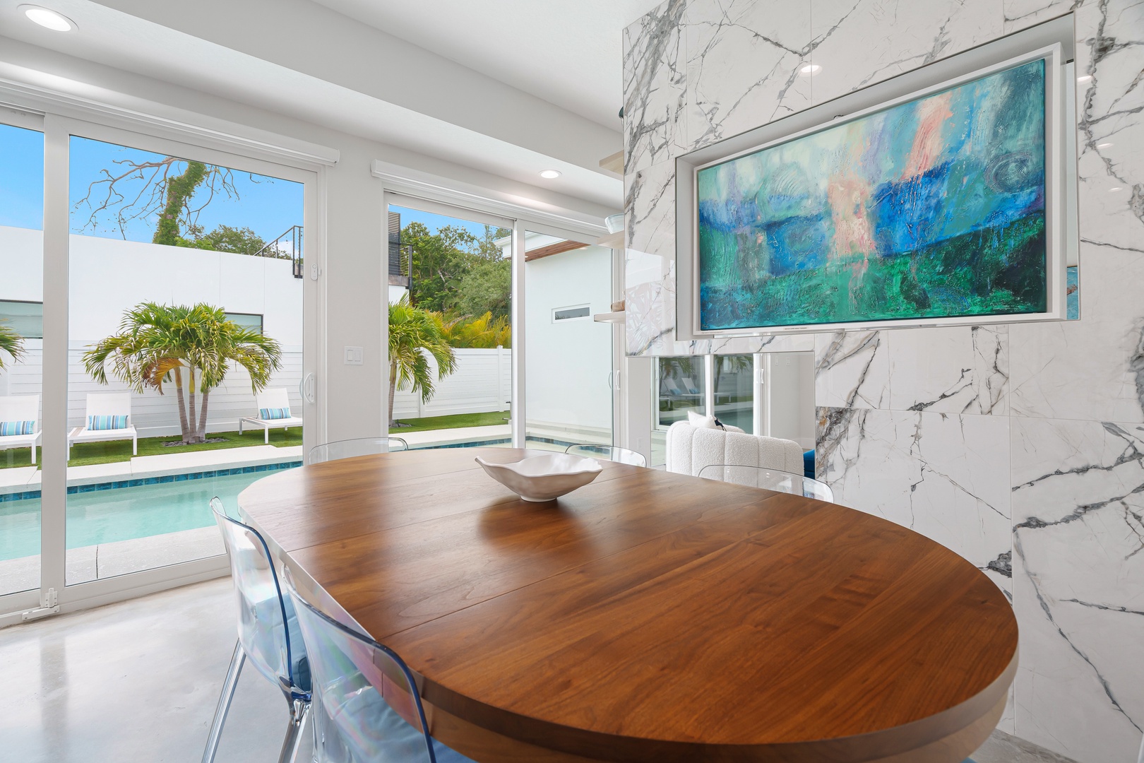 Step into a bright, elegant dining space with marble walls and a stunning round wood table. Just beyond, your private pool sparkles under tropical palms—where relaxation meets modern sophistication.