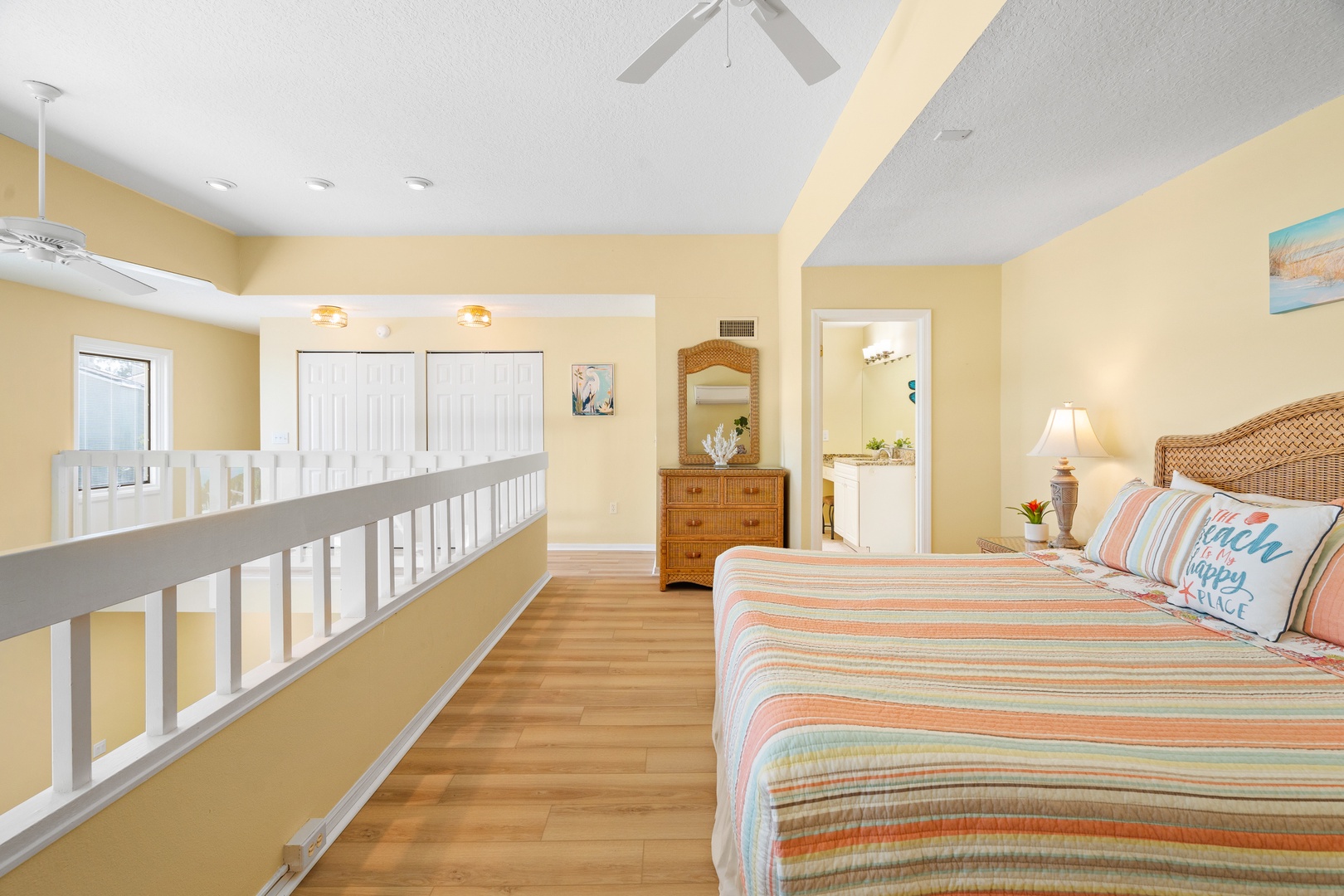 Your upstairs bedroom feels bright and airy with warm yellow walls, coastal bedding, and a ceiling fan for comfort.