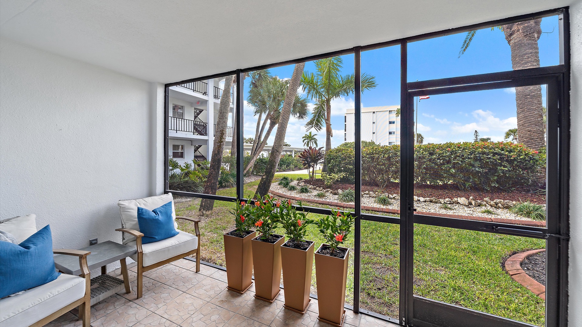 Relax in your screened-in patio with comfortable seating and fresh herb planters while enjoying garden views and tropical palms.