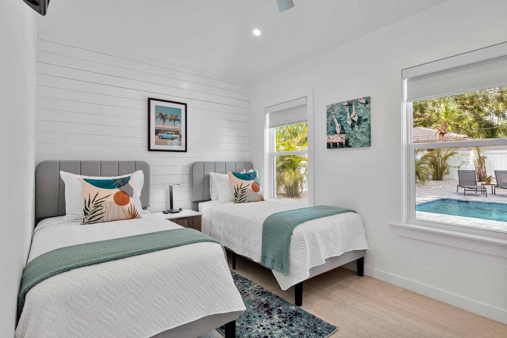 Wake to coastal artwork and sparkling pool views from your twin beds. Bright shiplap walls and teal accents create a breezy atmosphere perfect for restful mornings.