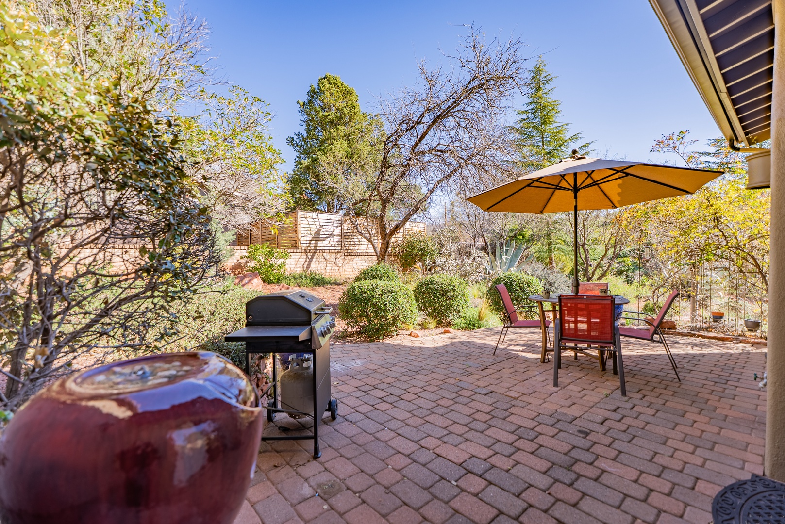 Your private patio awaits with brick flooring, shaded dining, and a BBQ grill surrounded by peaceful garden landscaping.