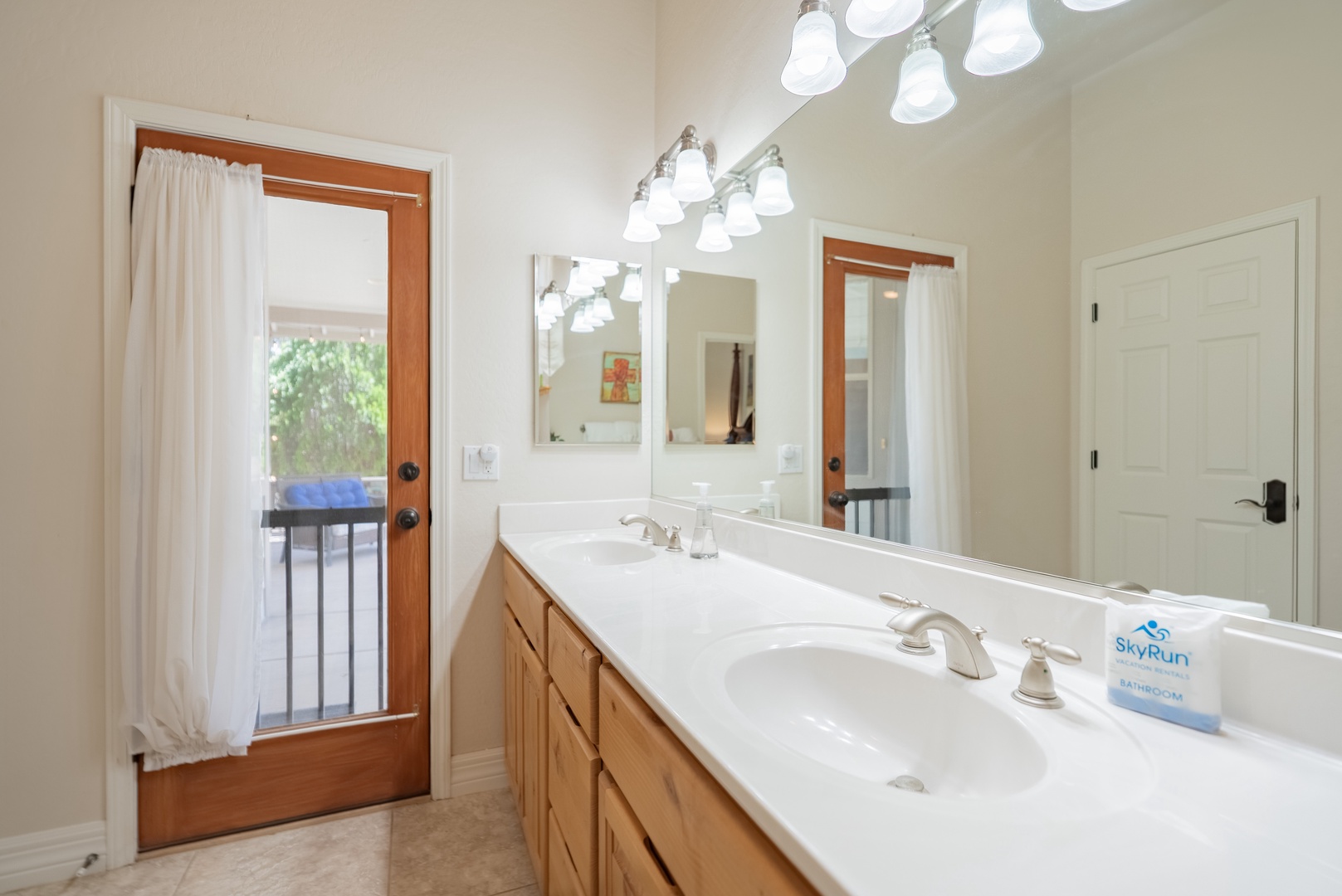Your spacious ensuite bathroom features dual vanities with warm wood cabinetry, perfect lighting, and French doors opening to your private outdoor space.