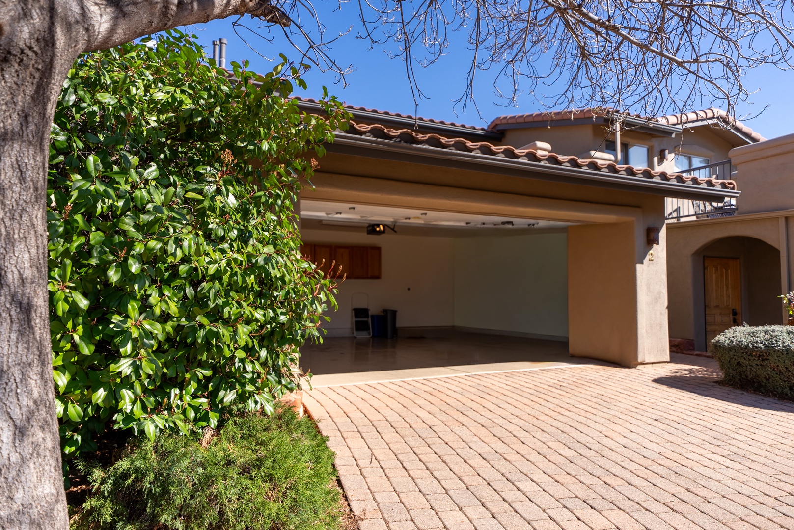 Mediterranean-style property features a spacious covered carport with terra cotta tile roofing and brick paver driveway surrounded by lush landscaping.