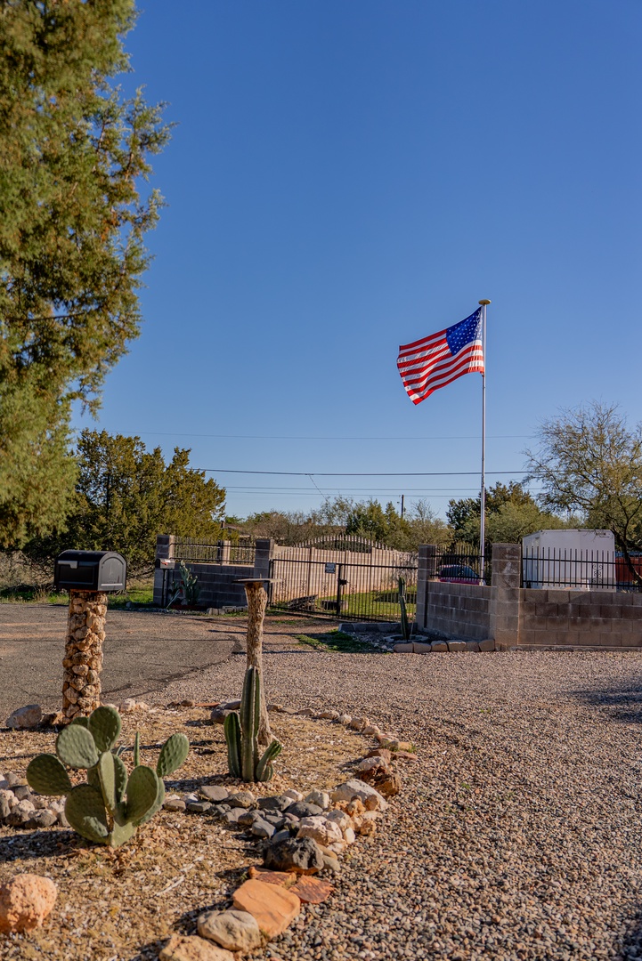 Property entrance features desert landscaping with cacti and an American flag marking the location in a peaceful rural setting.