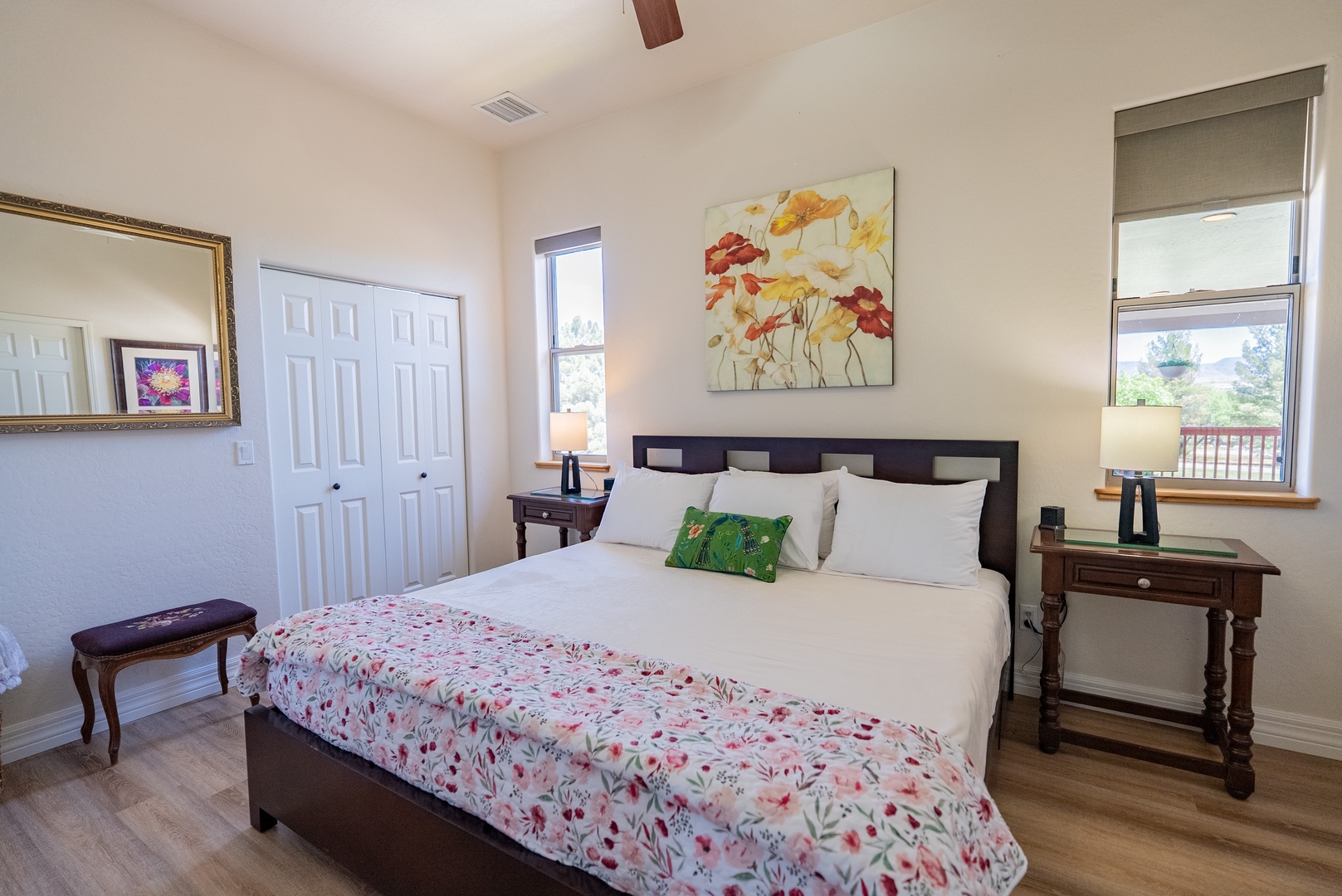 Relax in your bright bedroom featuring a cozy floral comforter and serene artwork, with natural light streaming through your windows.