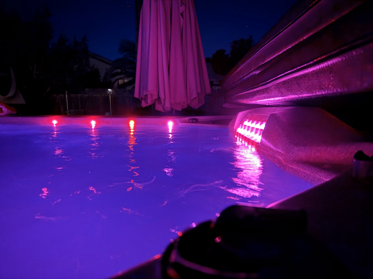Swimming pool illuminated with vibrant pink and purple lighting creates a magical nighttime atmosphere