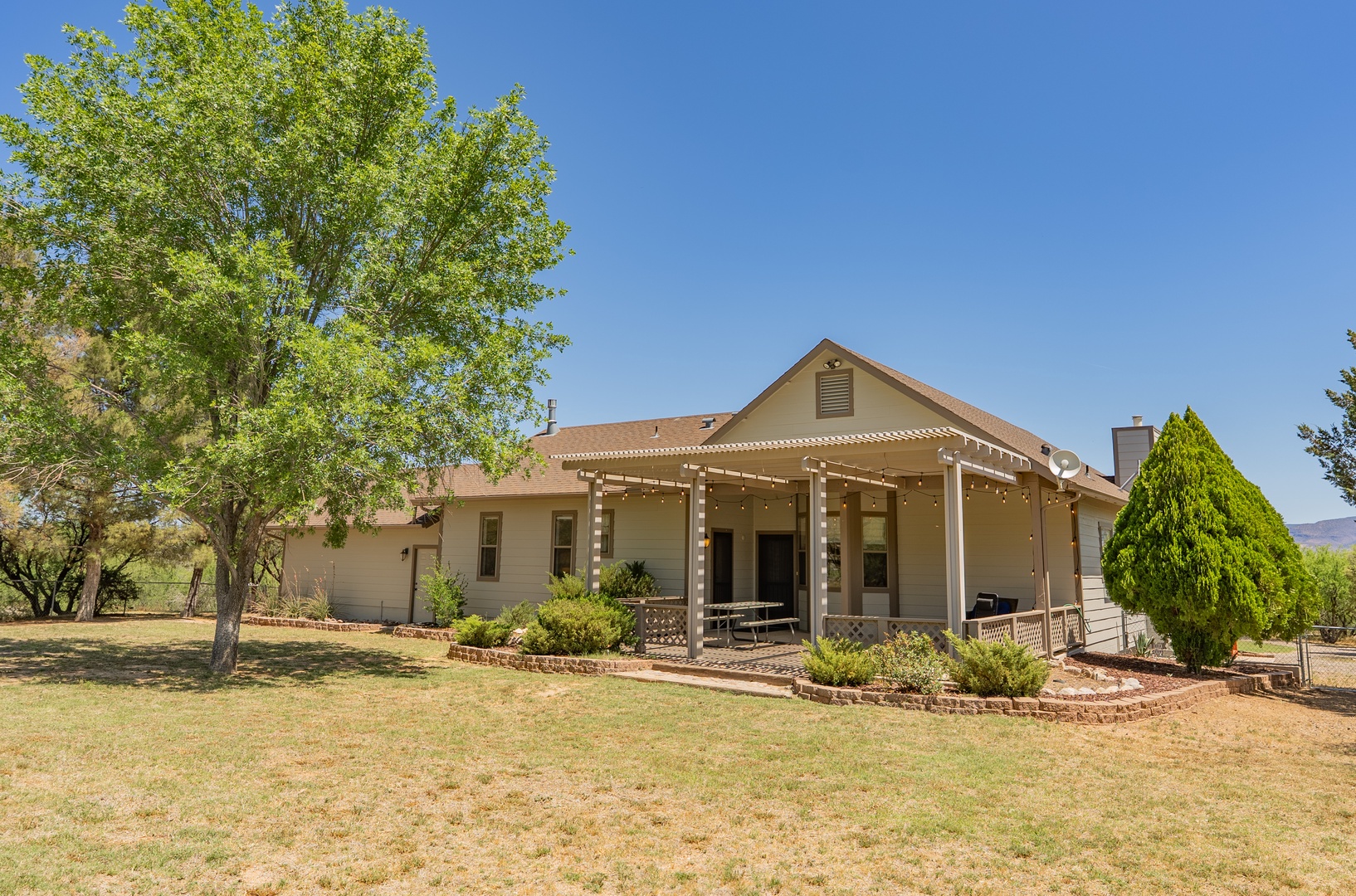 Charming property with covered porch featuring twinkling lights, nestled among mature trees on spacious grounds.