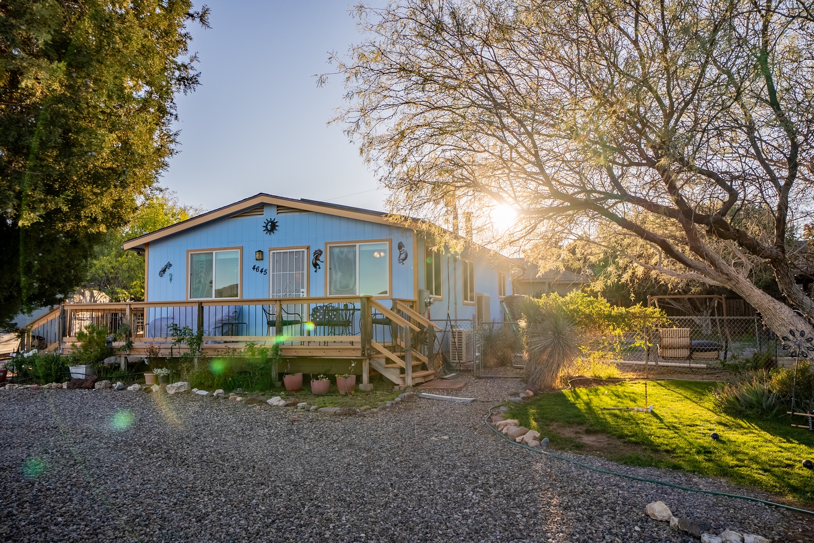 Charming blue property exterior nestled among mature trees with gravel driveway and welcoming front porch entrance.