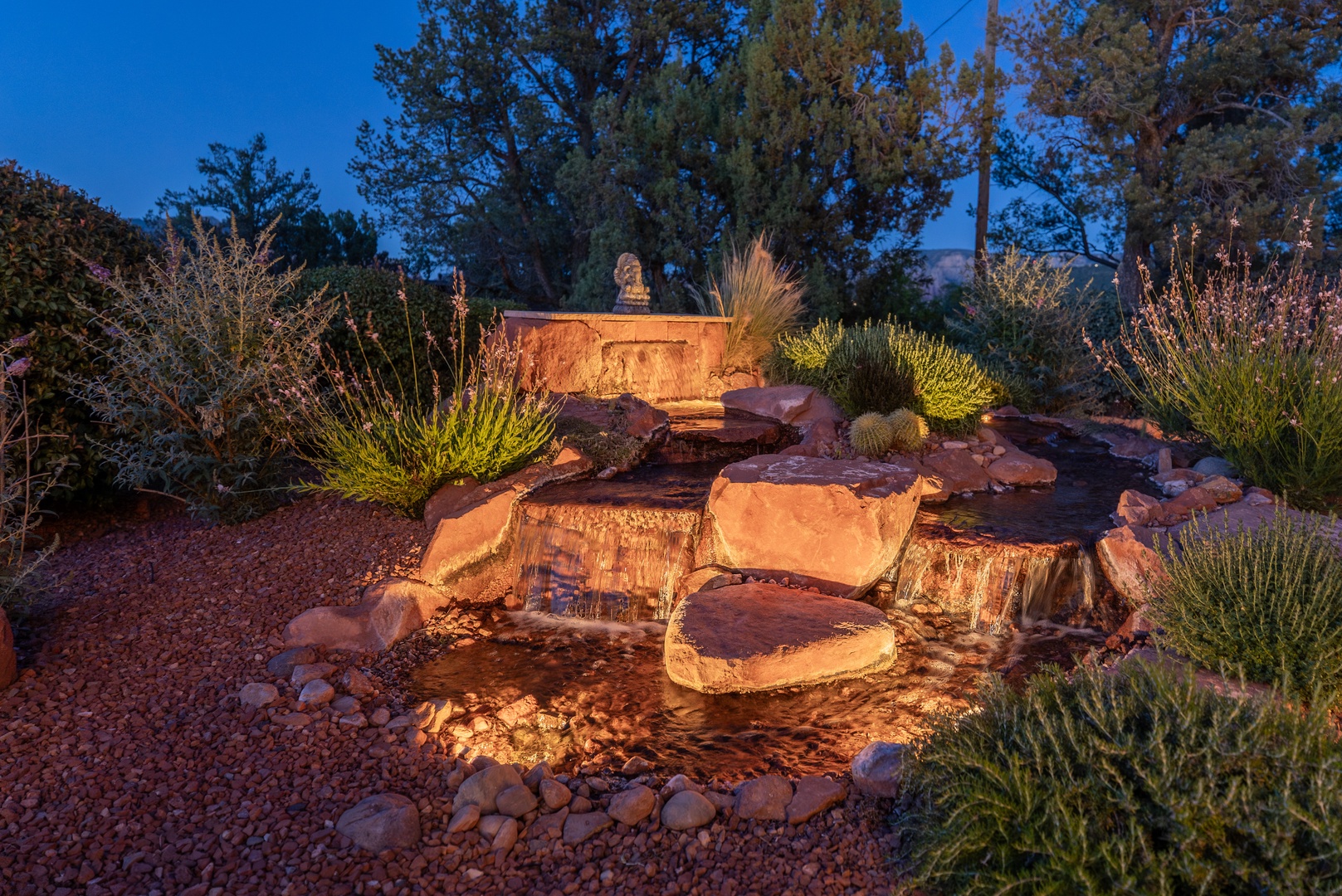 A softly lit water feature nestled among red rock and native desert plants