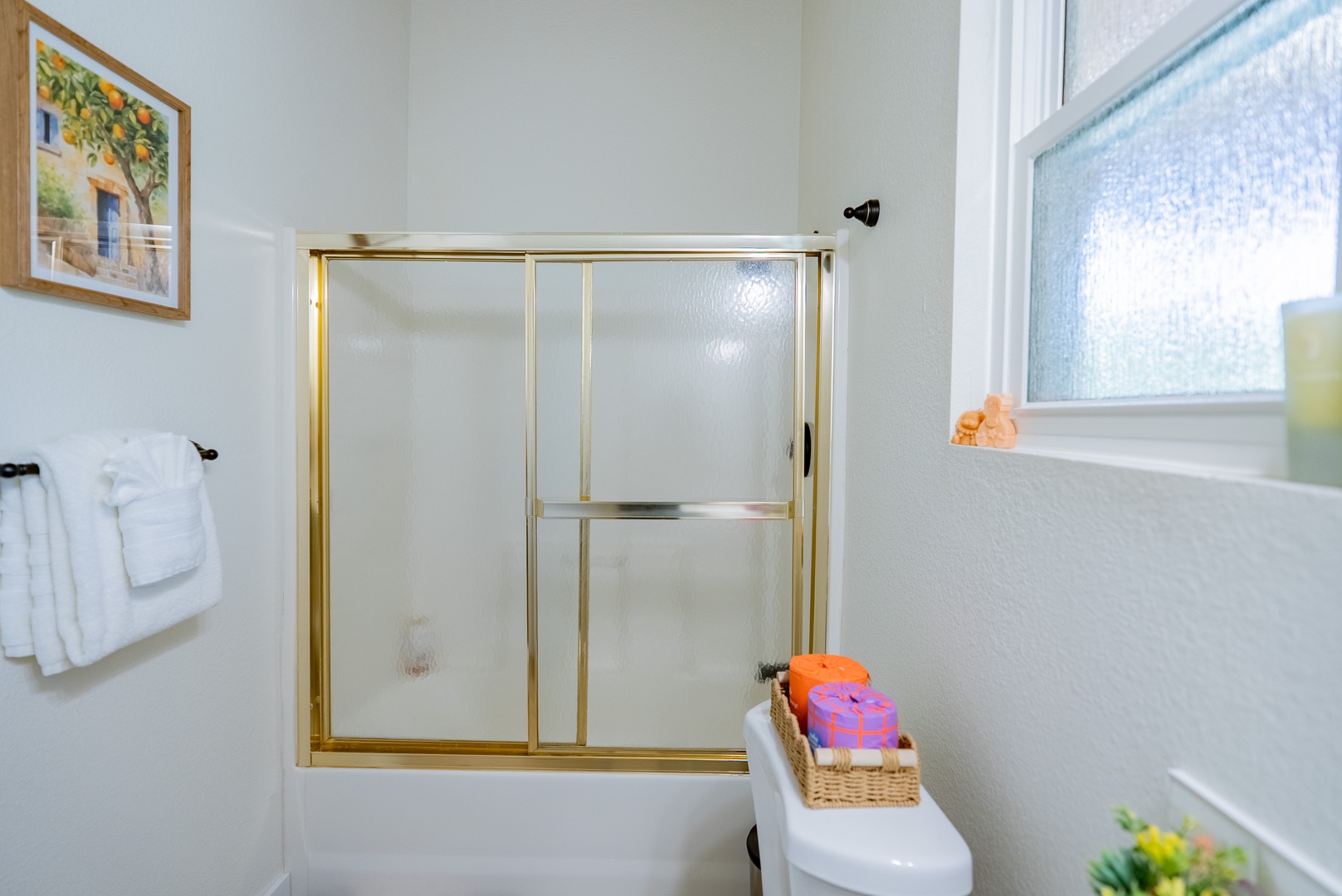 Your bright private bathroom features a tub-shower combo with frosted glass doors, fluffy white towels, and thoughtful amenities for a comfortable stay.