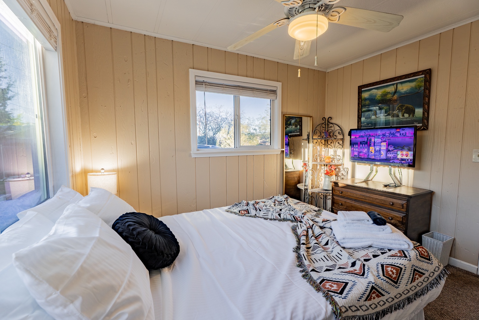 Unwind in this cozy bedroom featuring rustic wood-paneled walls, a comfortable bed with stylish throw blanket, and your own entertainment center with TV for relaxing evenings.
