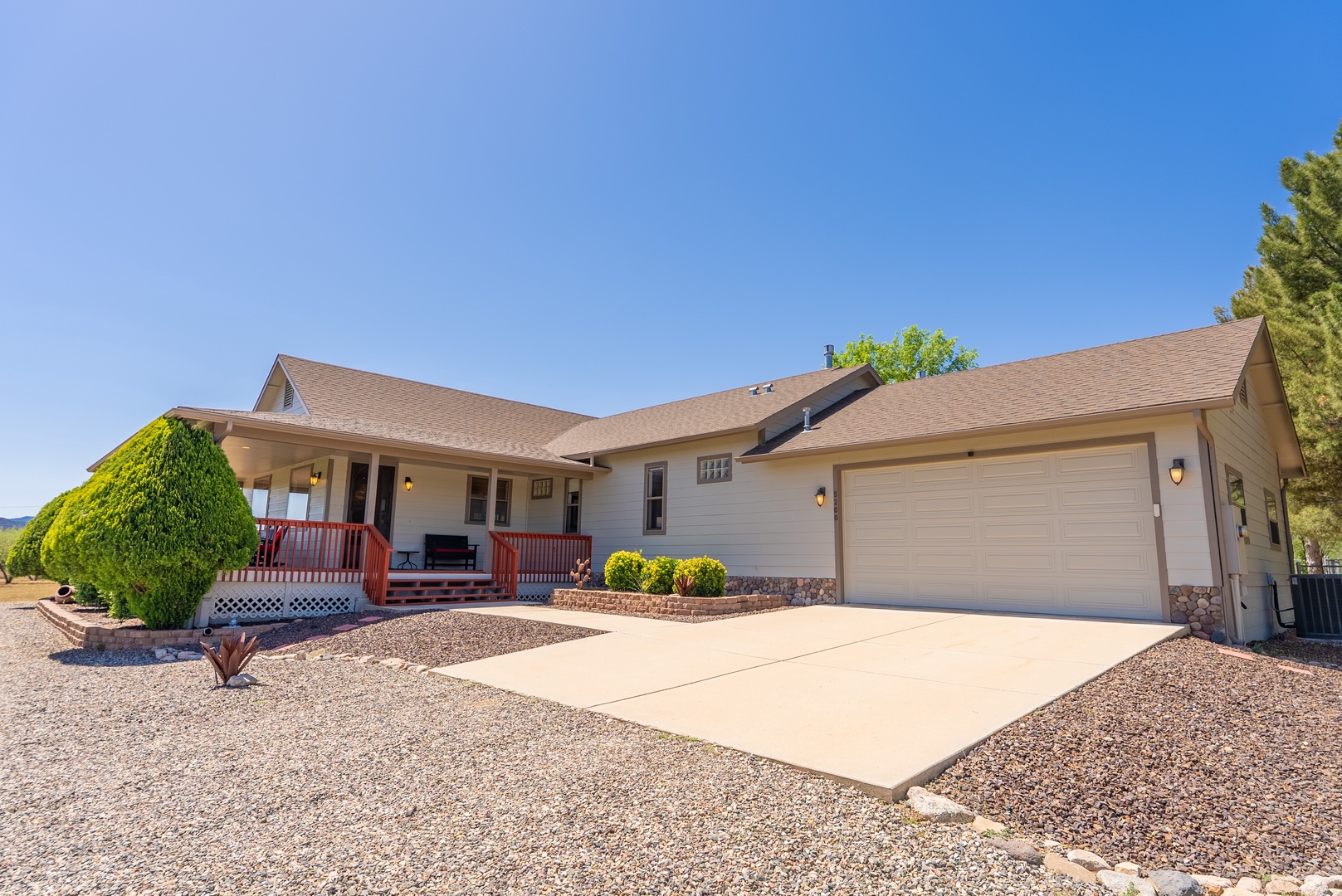 Spacious single-story home with welcoming front porch, attached garage, and desert landscaping under clear blue skies.