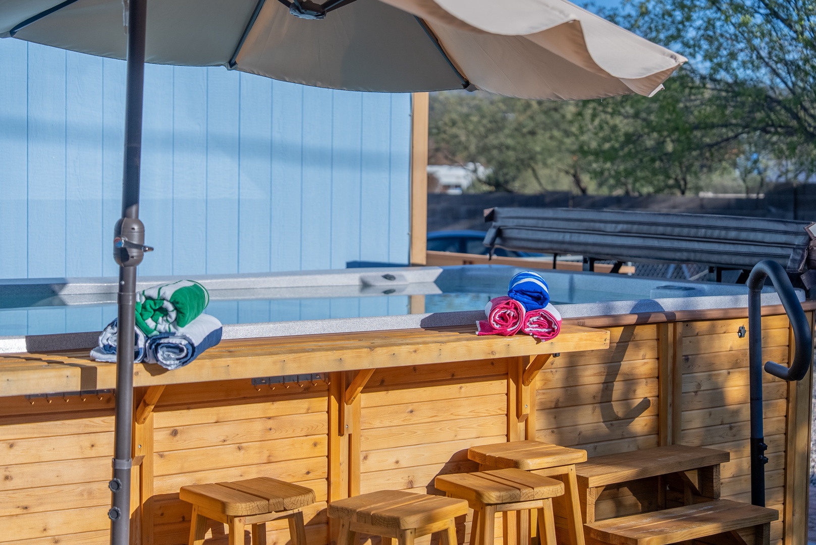 Relax poolside on comfortable wooden bar stools with colorful towels ready for your swim. The shaded seating area offers the perfect spot to unwind.